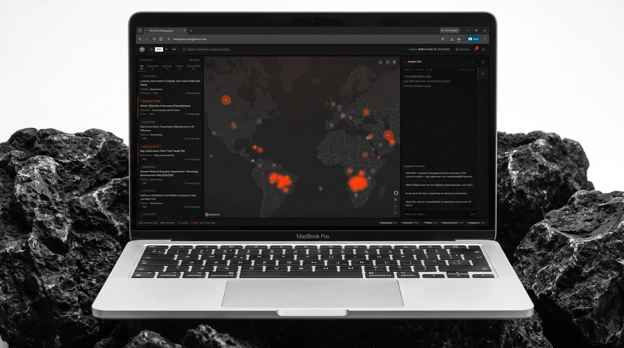 A silver MacBook Pro laptop displaying a world map with red and orange data points on a black background, surrounded by black rocks.