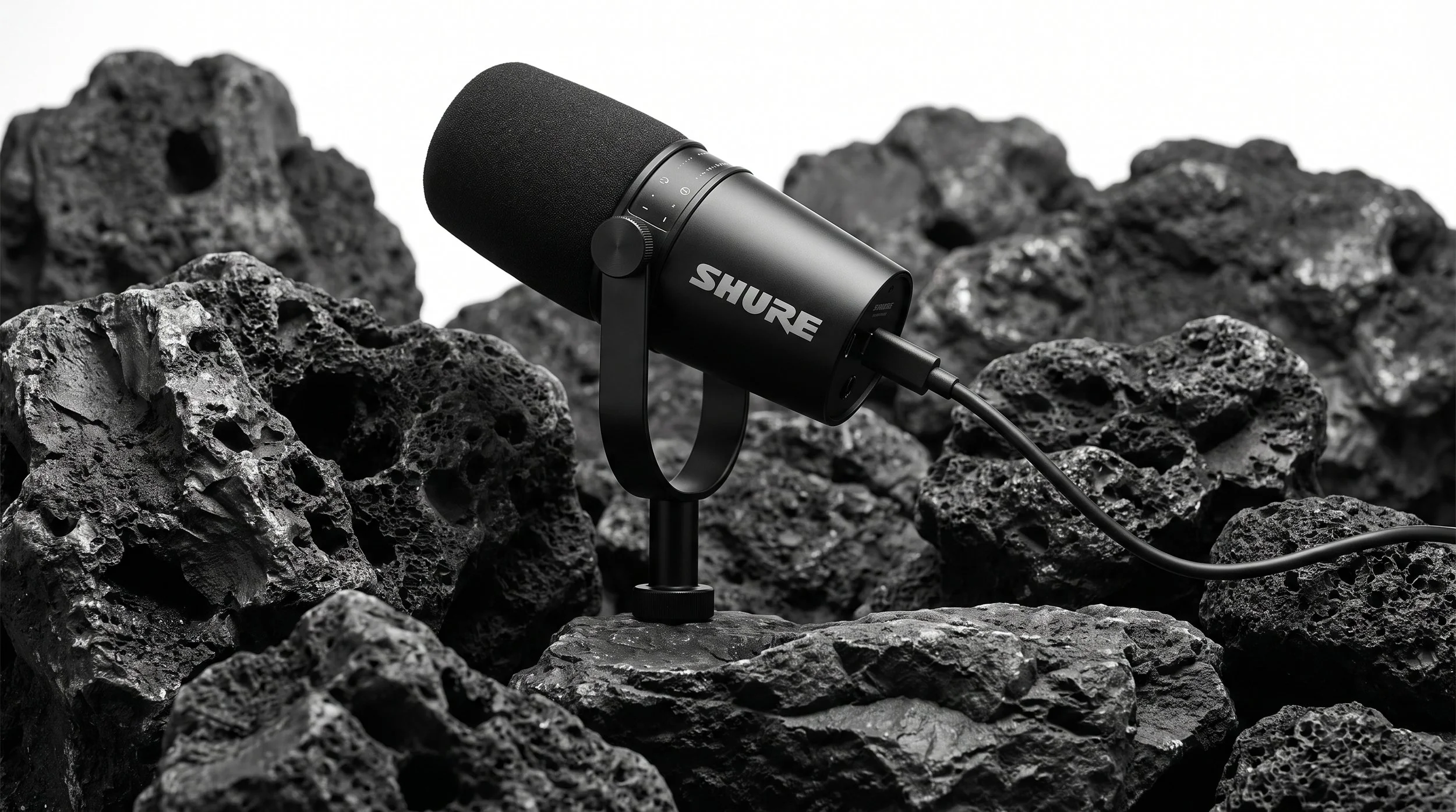 A black Shure microphone on a stand among rough volcanic rocks, with a white background.