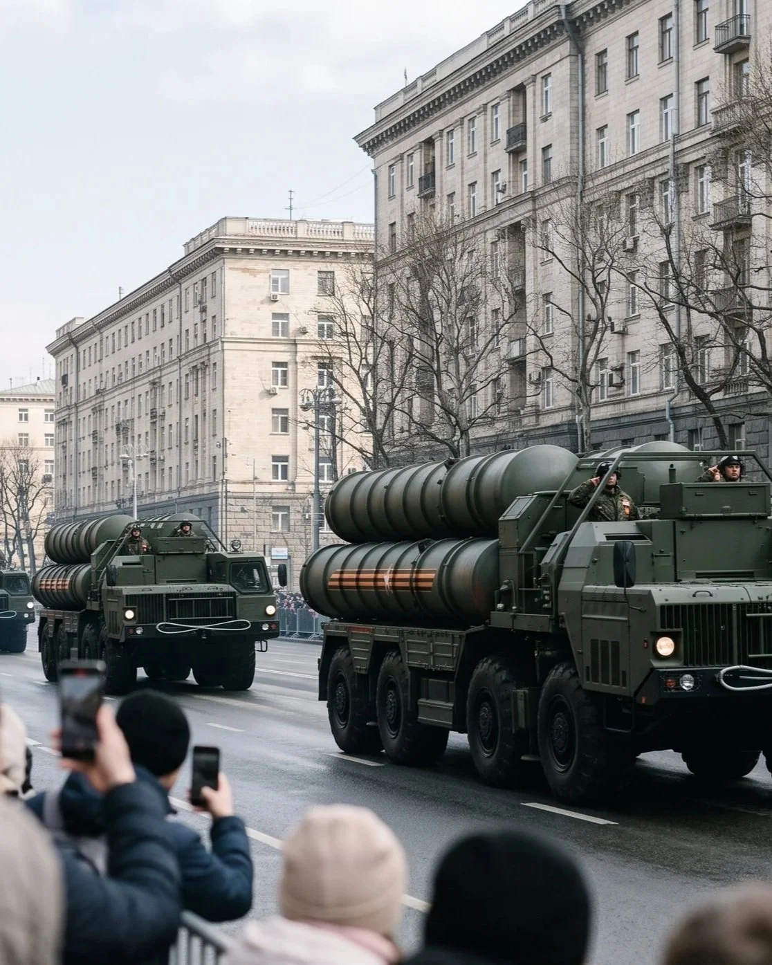 Military trucks carrying missile launchers passing through a city street with onlookers taking photos.