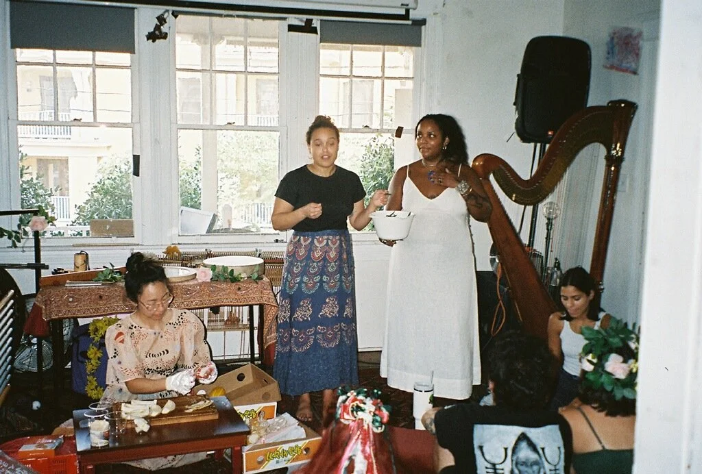 Women gathered in community with Alexis Sāga for a ceremonial celebration, accompanied by live harp music.