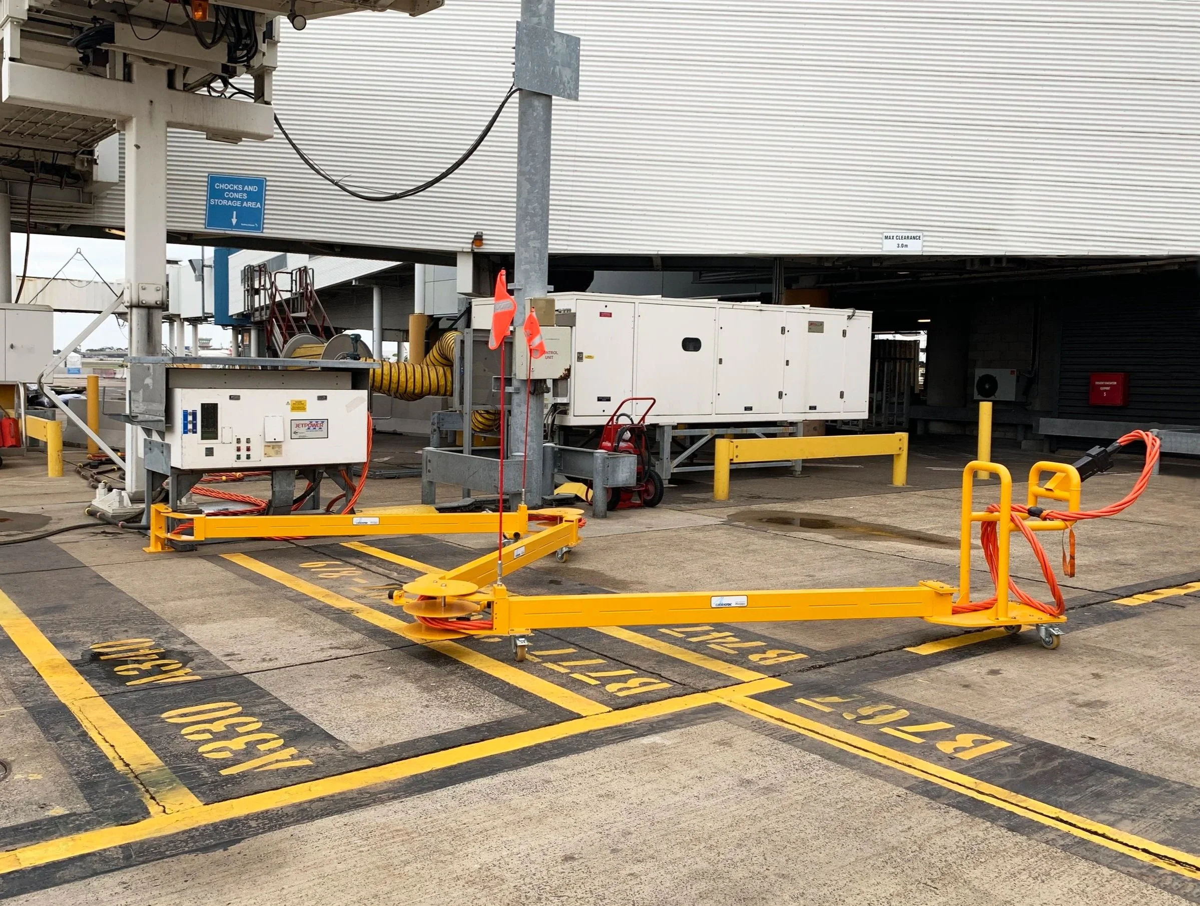 Airport tarmac with equipment and markings, including a large white ground power unit and various hoses. There is a yellow CableCroc unit in the foreground.