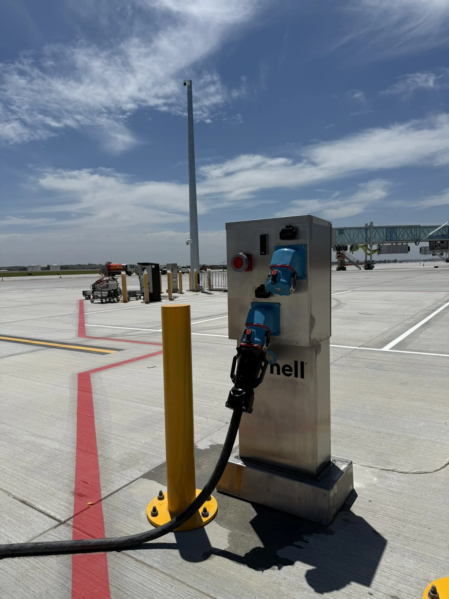 Dynell 400Hz Ground Power System on an airport tarmac, connected to something with a cord out of frame, under a partly cloudy sky.