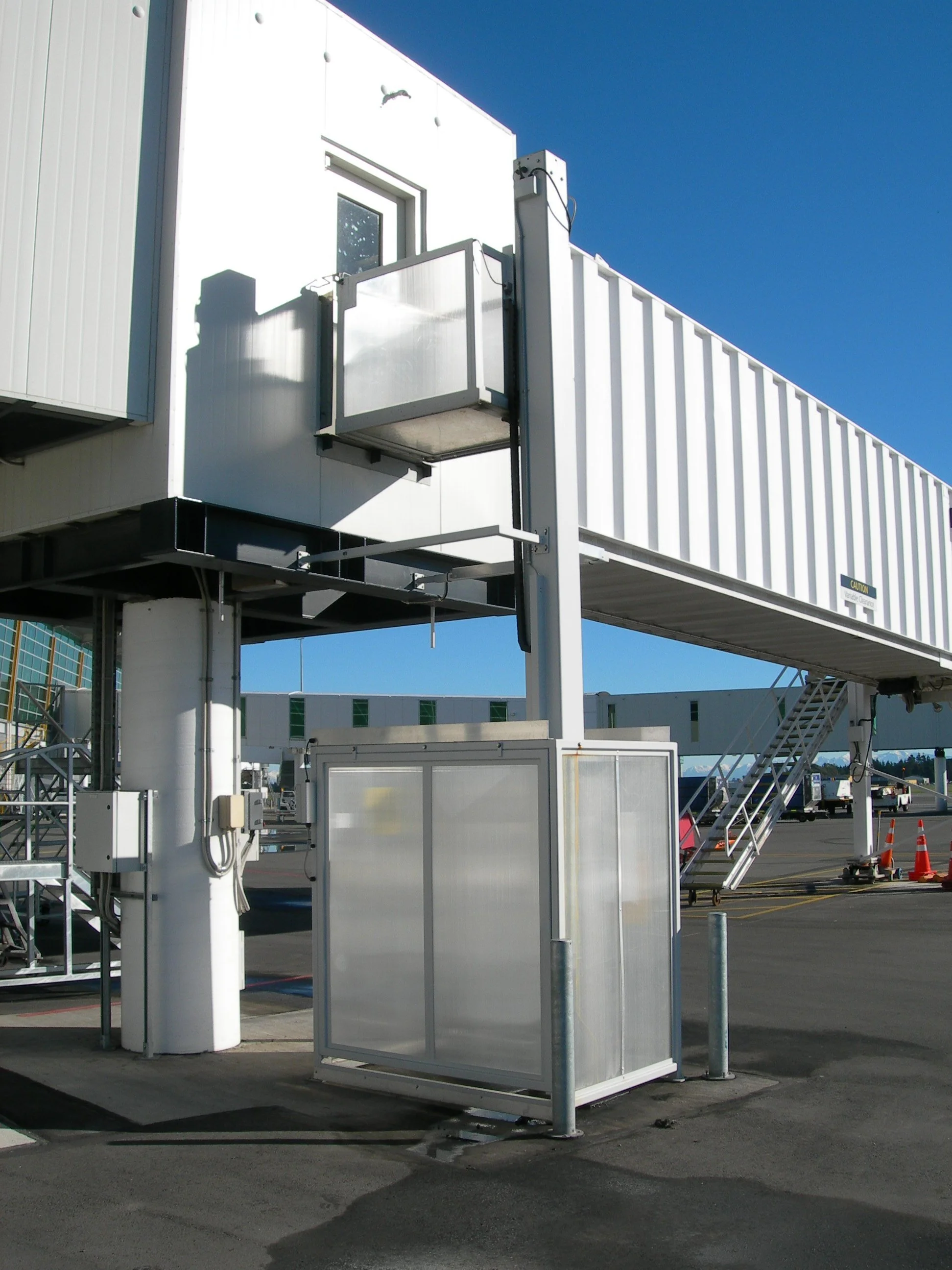 An empty baggage lift connected to a building and bridge outside under a clear blue sky.