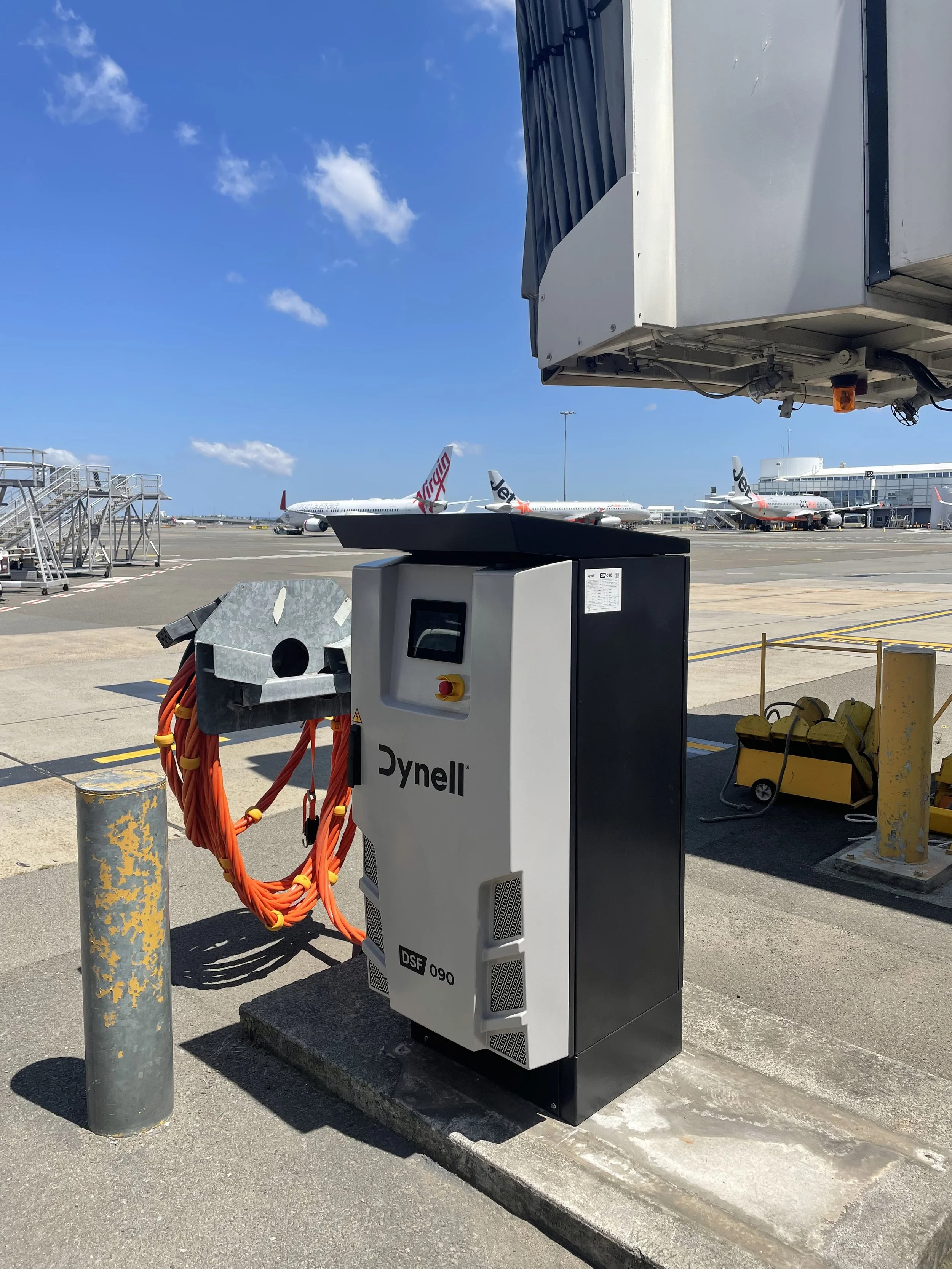 Airport tarmac with several Virgin and Jetstar airplanes in the background, with a Dynell 400Hz Ground Power System in the foreground.