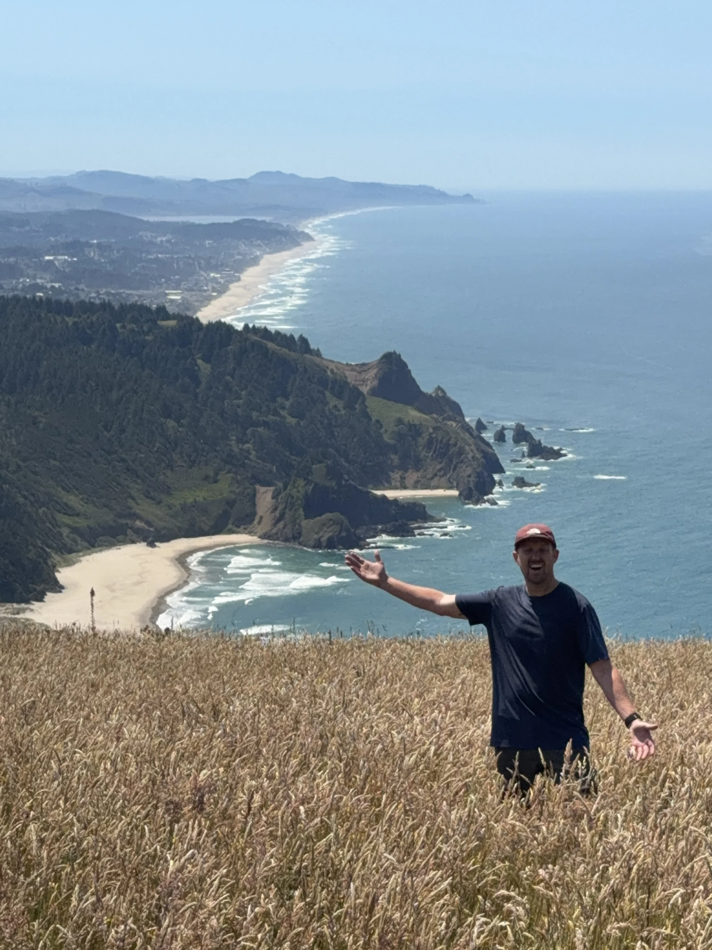 Schro standing in a golden field overlooking costal cliffs in Oregon along the Pacific Coast