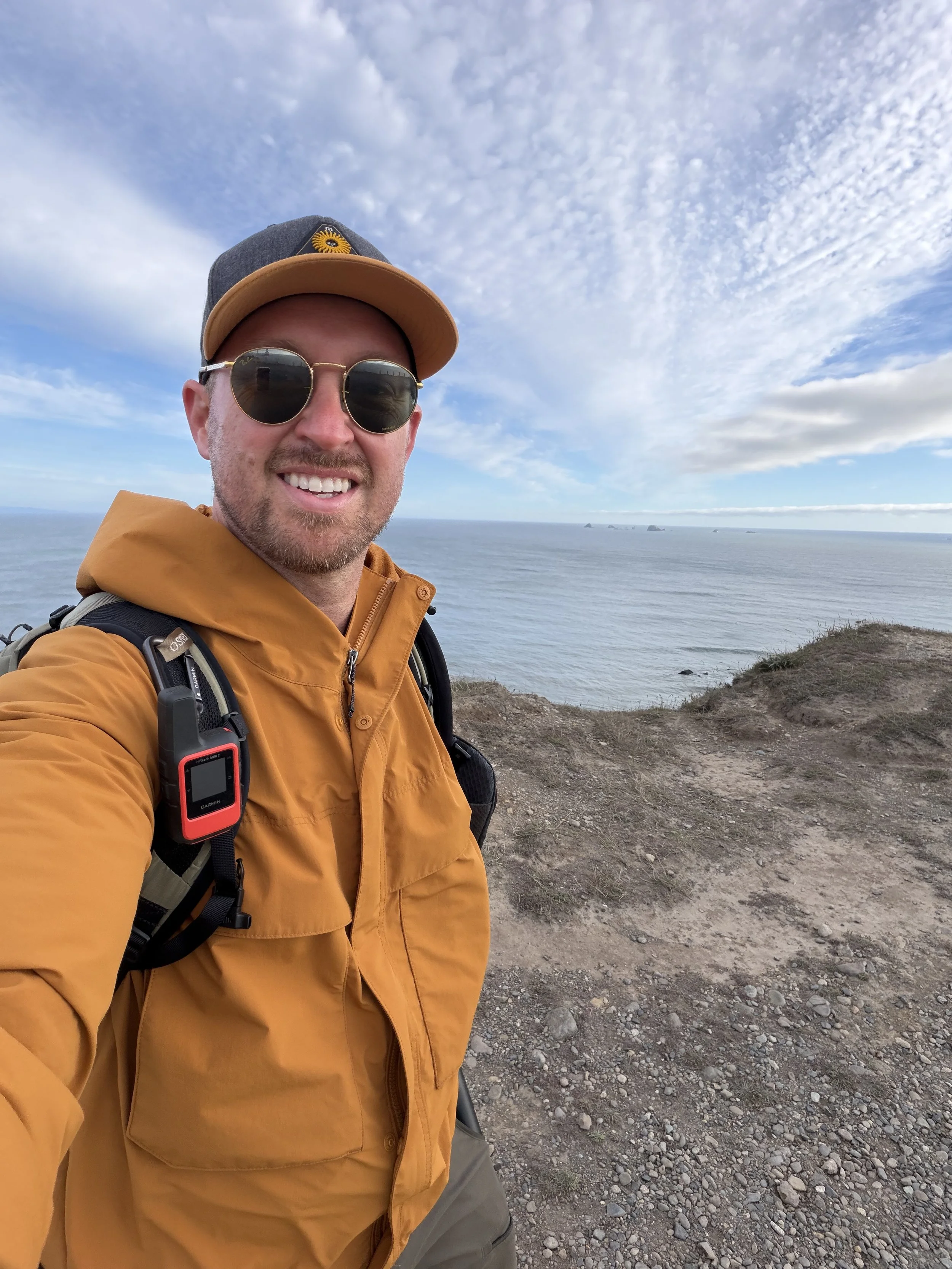 Schro smiling beside the scenic Pacific coastline in Oregon under a cloudy blue sky
