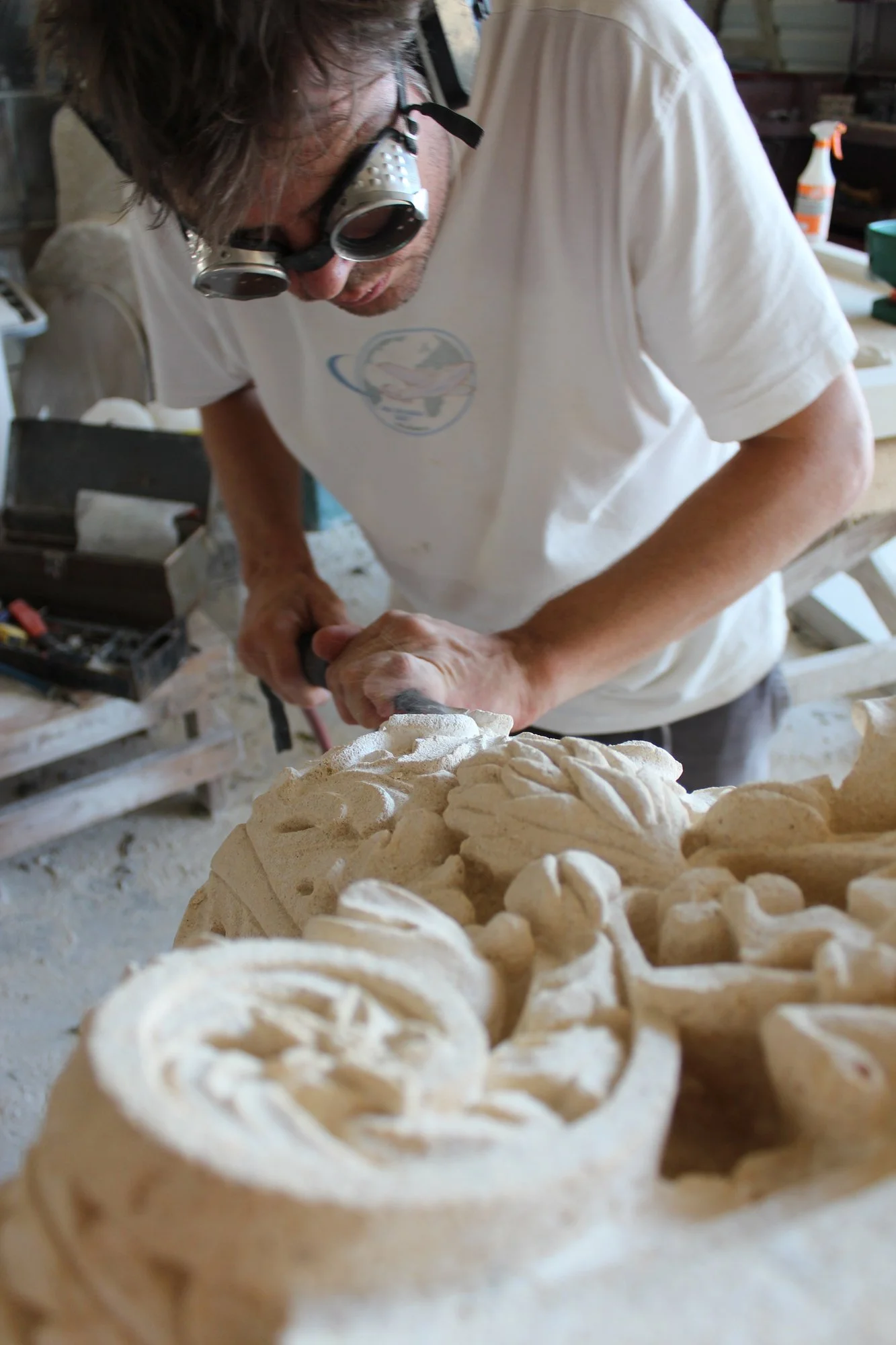 Matthew Johnson carving into a large piece of limestone with a pneumatic hammer, in the Bartlett Stone Carving workshop filled with tools and equipment.