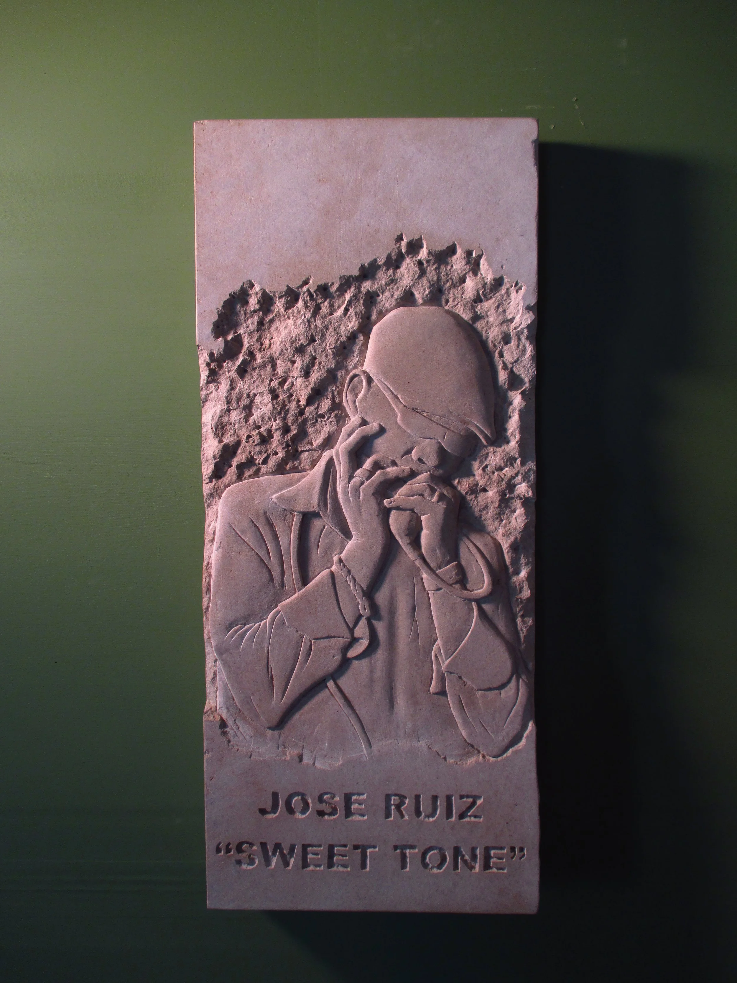 Carved stone relief musician playing the harmonica. The inscription below reads 'Jose Ruiz,' and underneath that, 'Sweet Tone'.