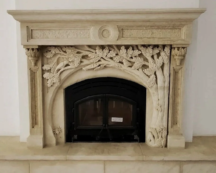 Ornate stone fireplace with detailed carvings of leafy branches and columns surrounding a black metal fire door.