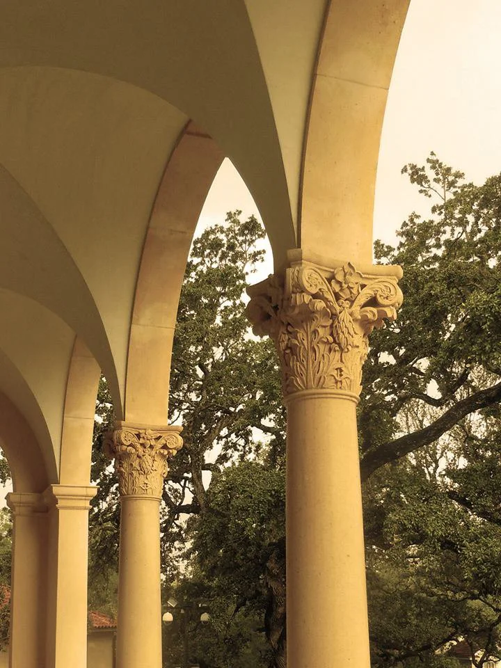 Classical stone columns with modified corinthian capitals supporting arches.