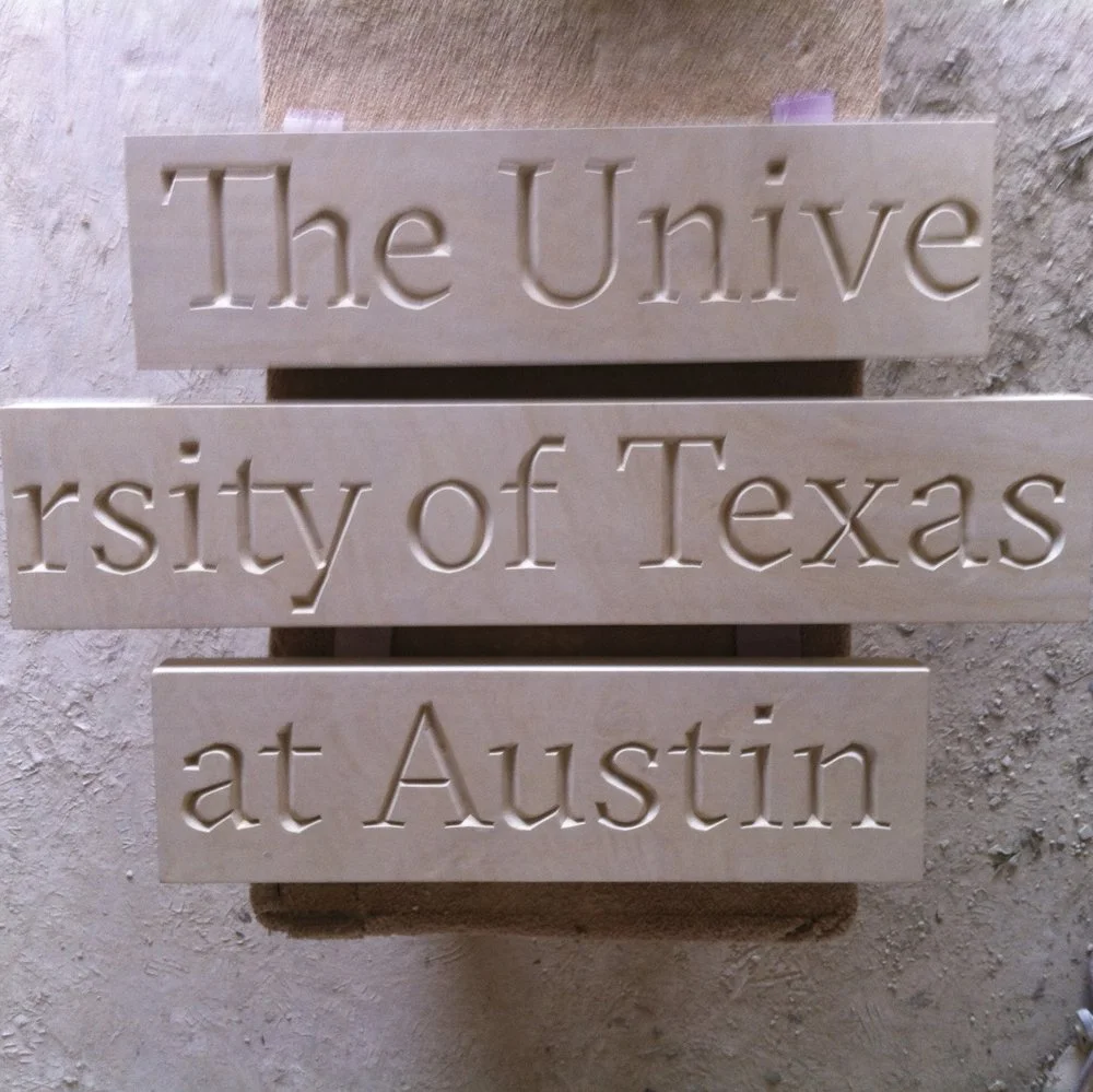 3 stone blocks with engraved text reading "The Unive", "rsity of Texas", and "at Austin" arranged to spell "The University of Texas at Austin".