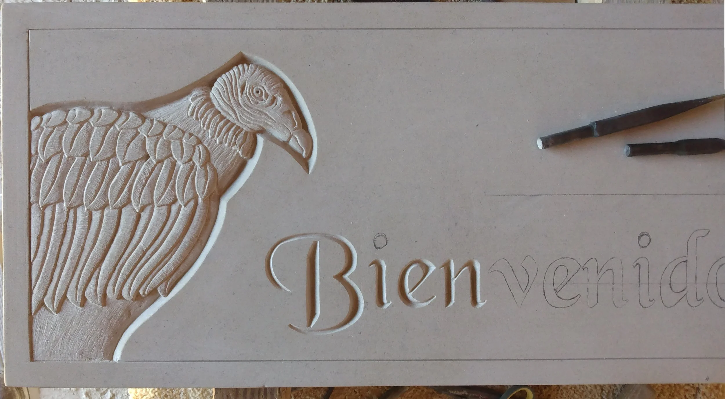 A carved stone sign in progress featuring a vulture and the partially completed word "Bienvenidos"