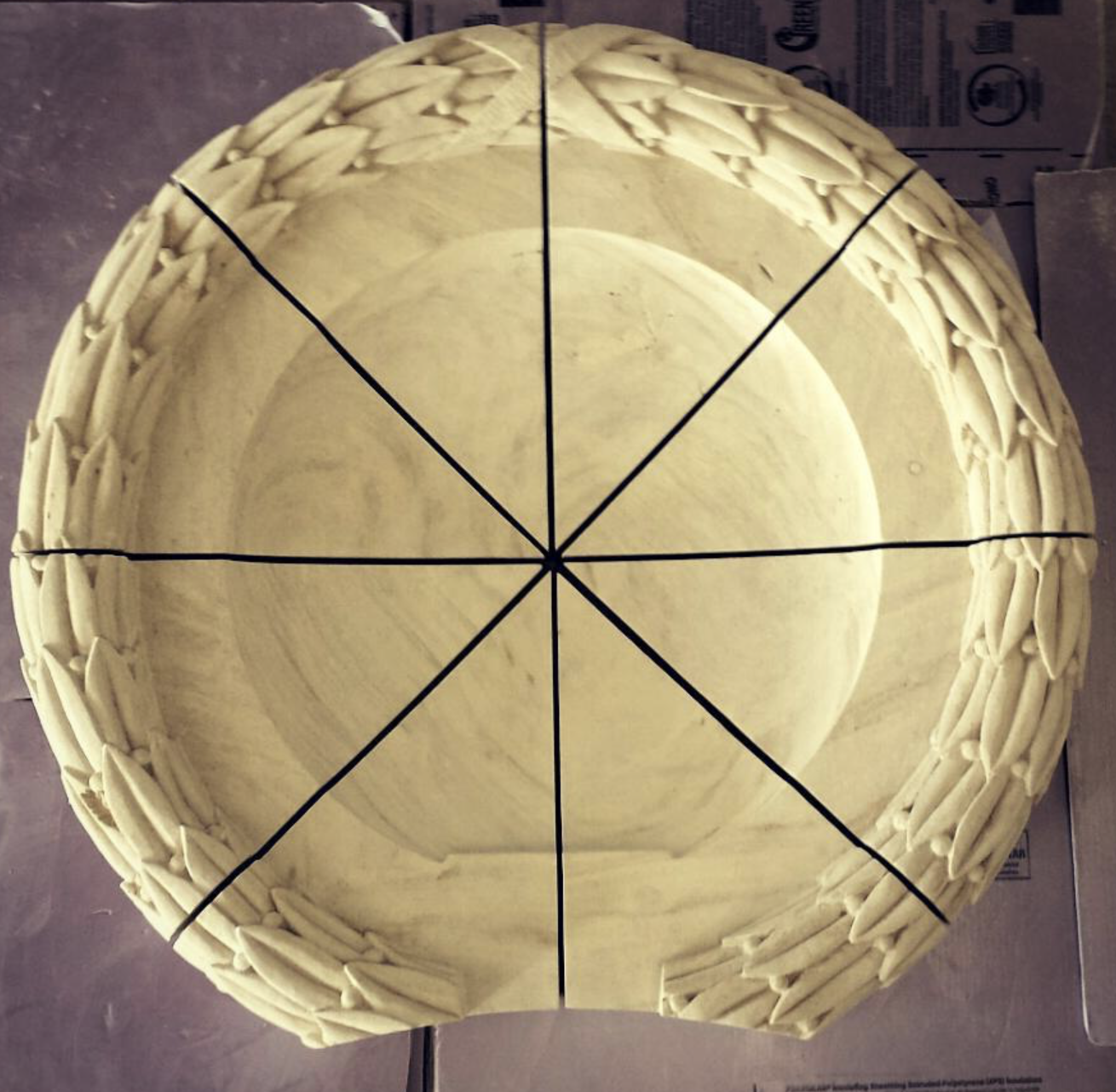 A large round wooden basket with a decorative braided rim, divided into eight segments with black lines.
