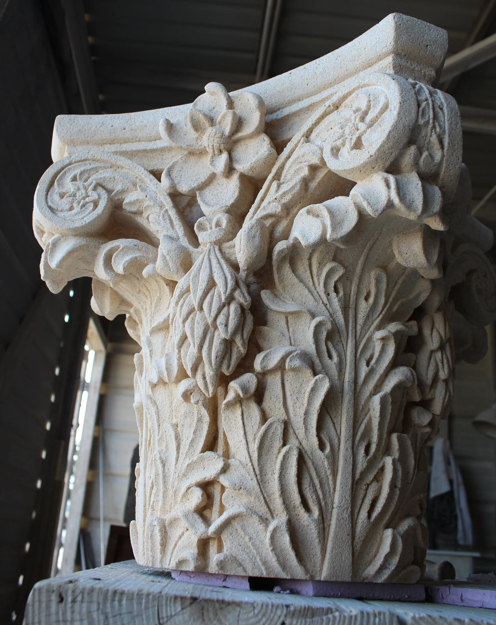 An elaborately carved stone modified corinthian capital with floral and scroll motifs
