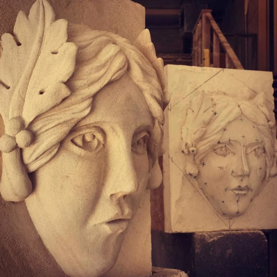 A carved stone sculpture of a woman's face with detailed hair, accompanied by a work-in-progress version with guidelines and marks for carving.