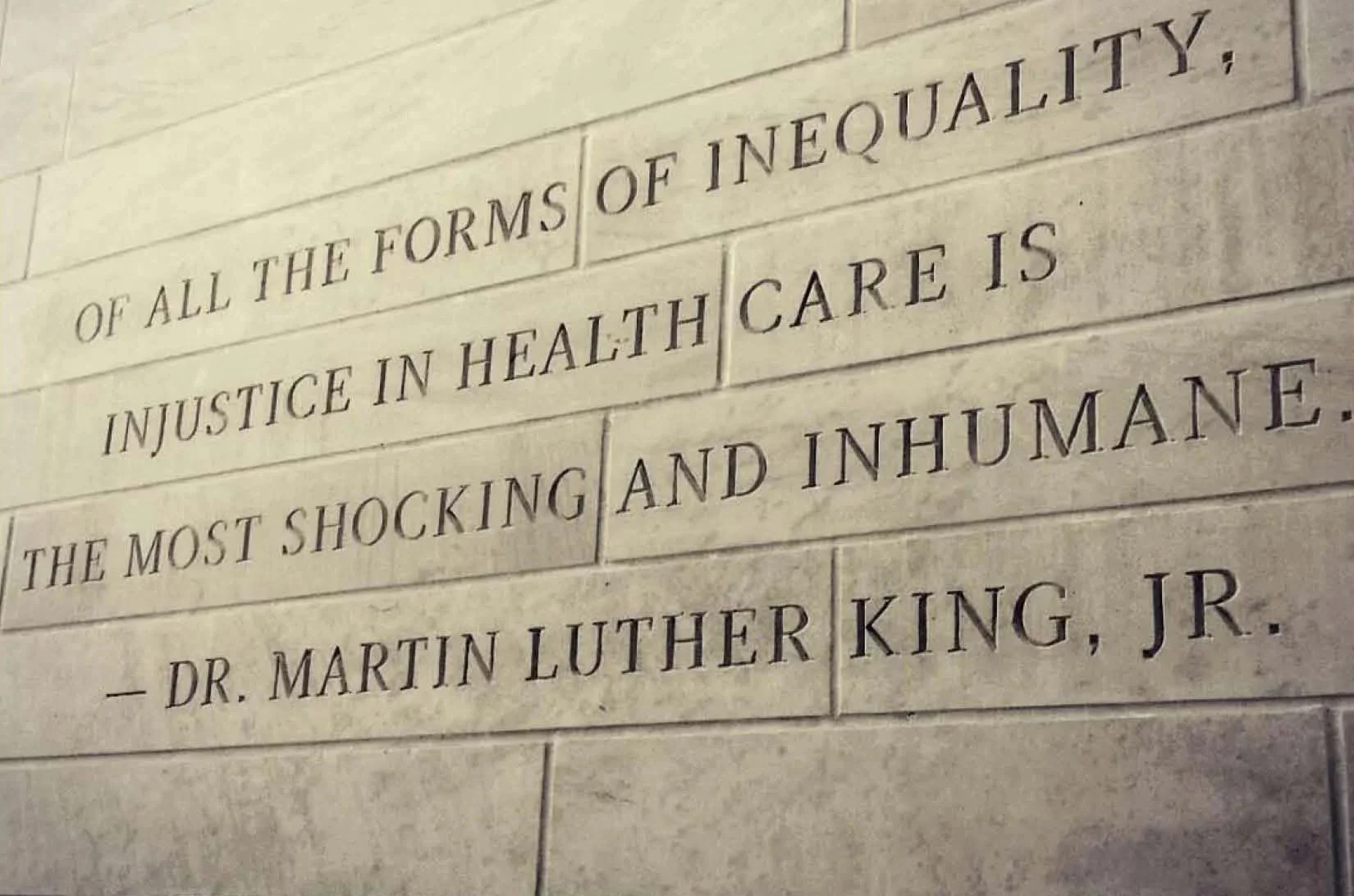 A stone wall with engraved quote attributed to Dr. Martin Luther King, Jr., emphasizing inequality and healthcare.