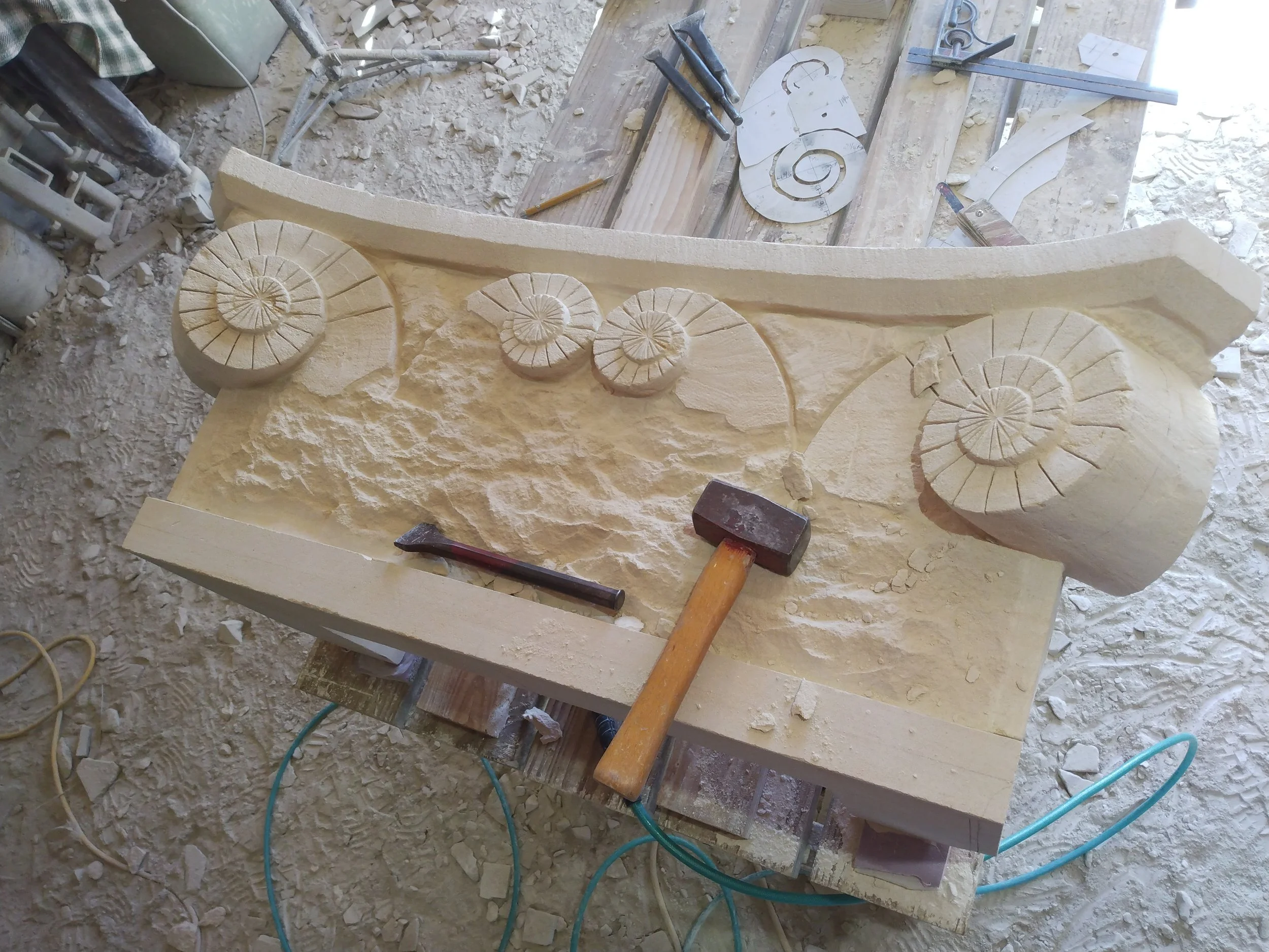 Bartlett Stone Carving workshop with carved spiral shell design patterns on a large piece of limestone, surrounded by tools and dust.