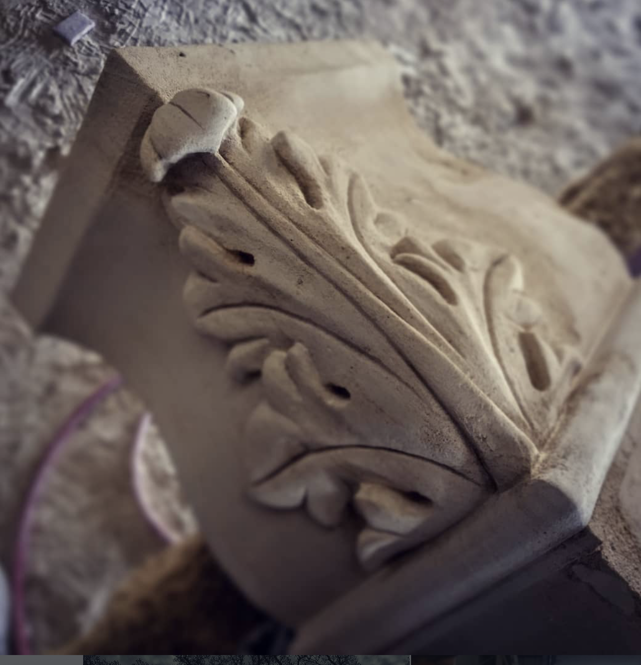 Close-up of an ornate carved stone block with floral and leaf patterns in beige and light brown tones.