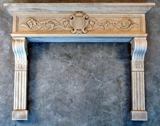 Decorative limestone fireplace mantel with carved detailing and fluted columns on a stone wall.