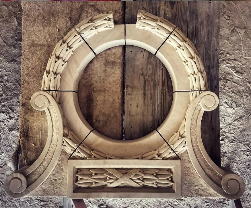 Ornate carved limestone window surround with scroll-shaped sides and detailed carvings at the bottom.