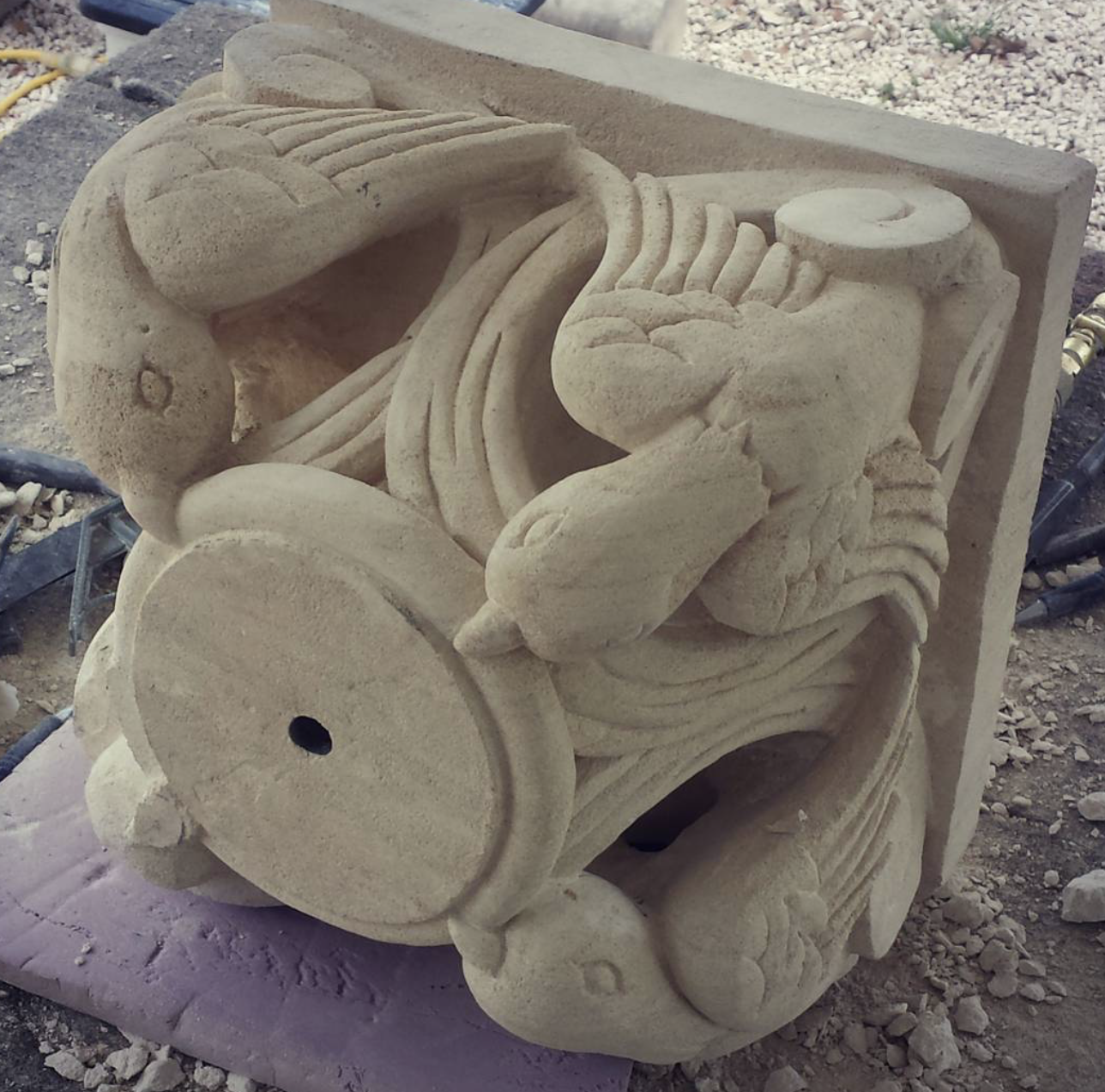 Sandstone sculpture of two fish with flowing water and wave patterns, possibly part of a fountain or decorative piece.