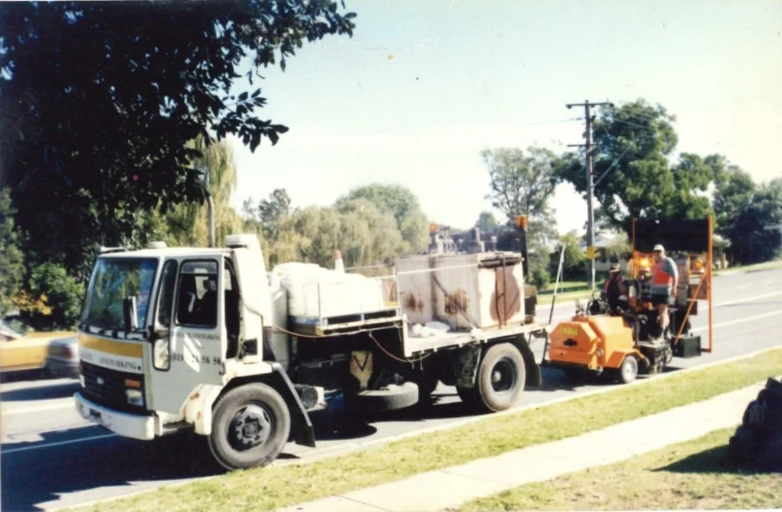 Street maintenance truck with orange equipment and workers working on the roadside.