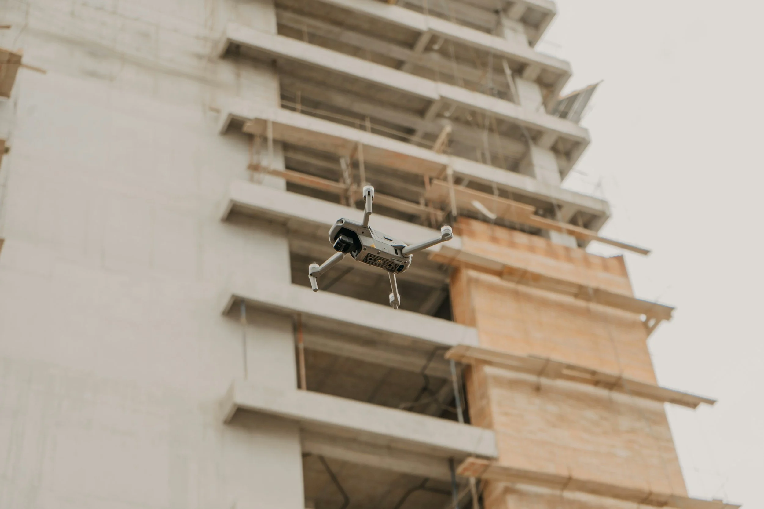 A drone flying near the construction of a building with multiple floors and exposed wooden beams.