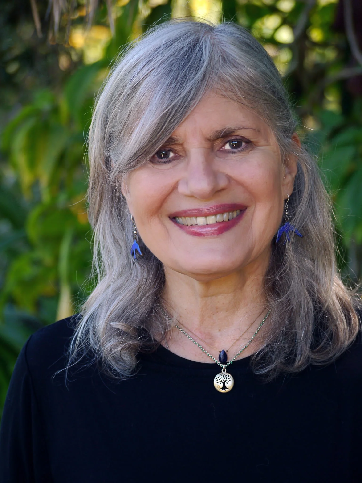 A woman in her 60s (Betsy Mars), smiling at the camera with a verdant green background