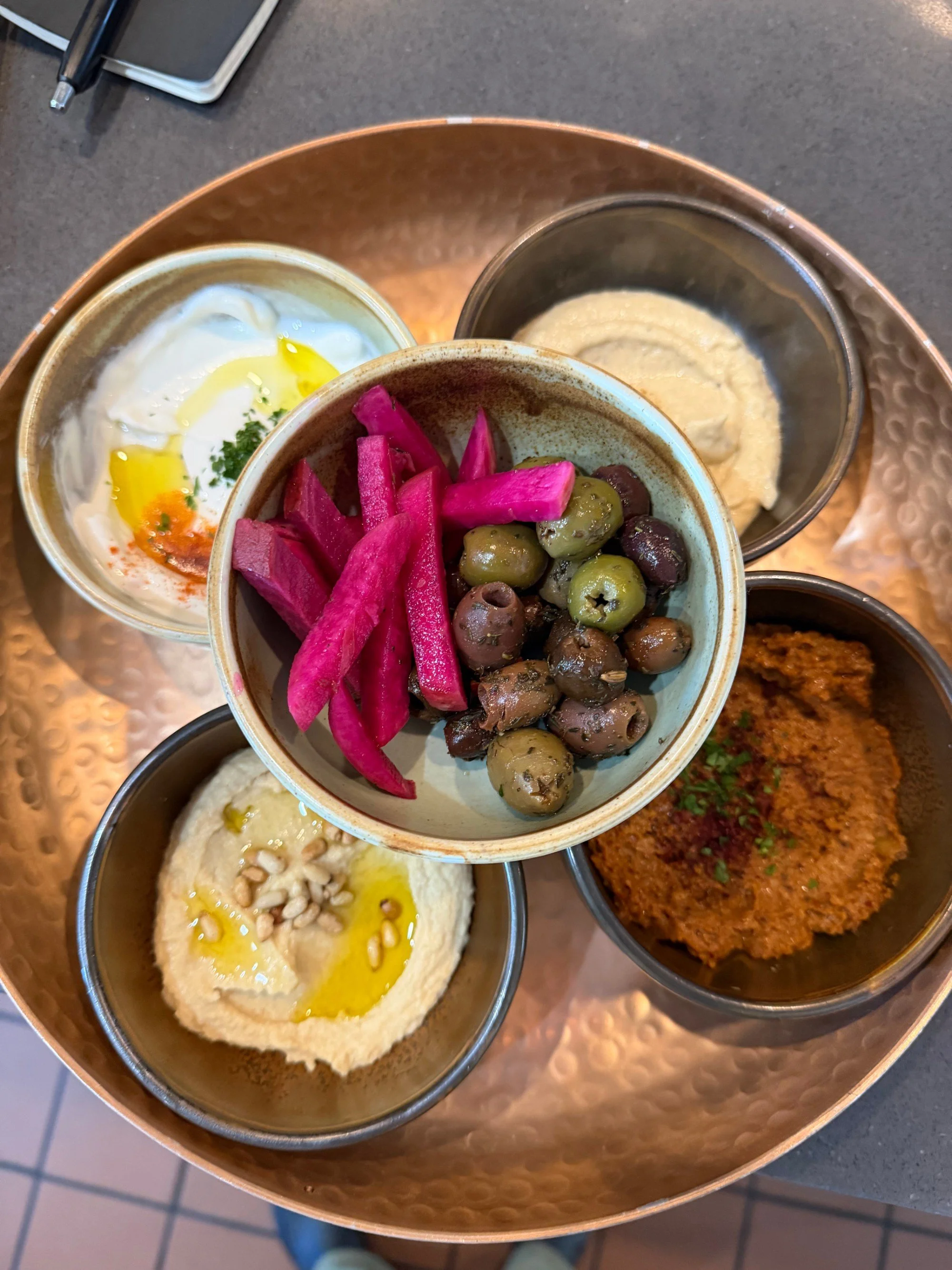 Mezze at Bacchus Kitchen seen from above — hummus, baba ghanouj, muhammara, olives and pickled turnip on a copper tray
