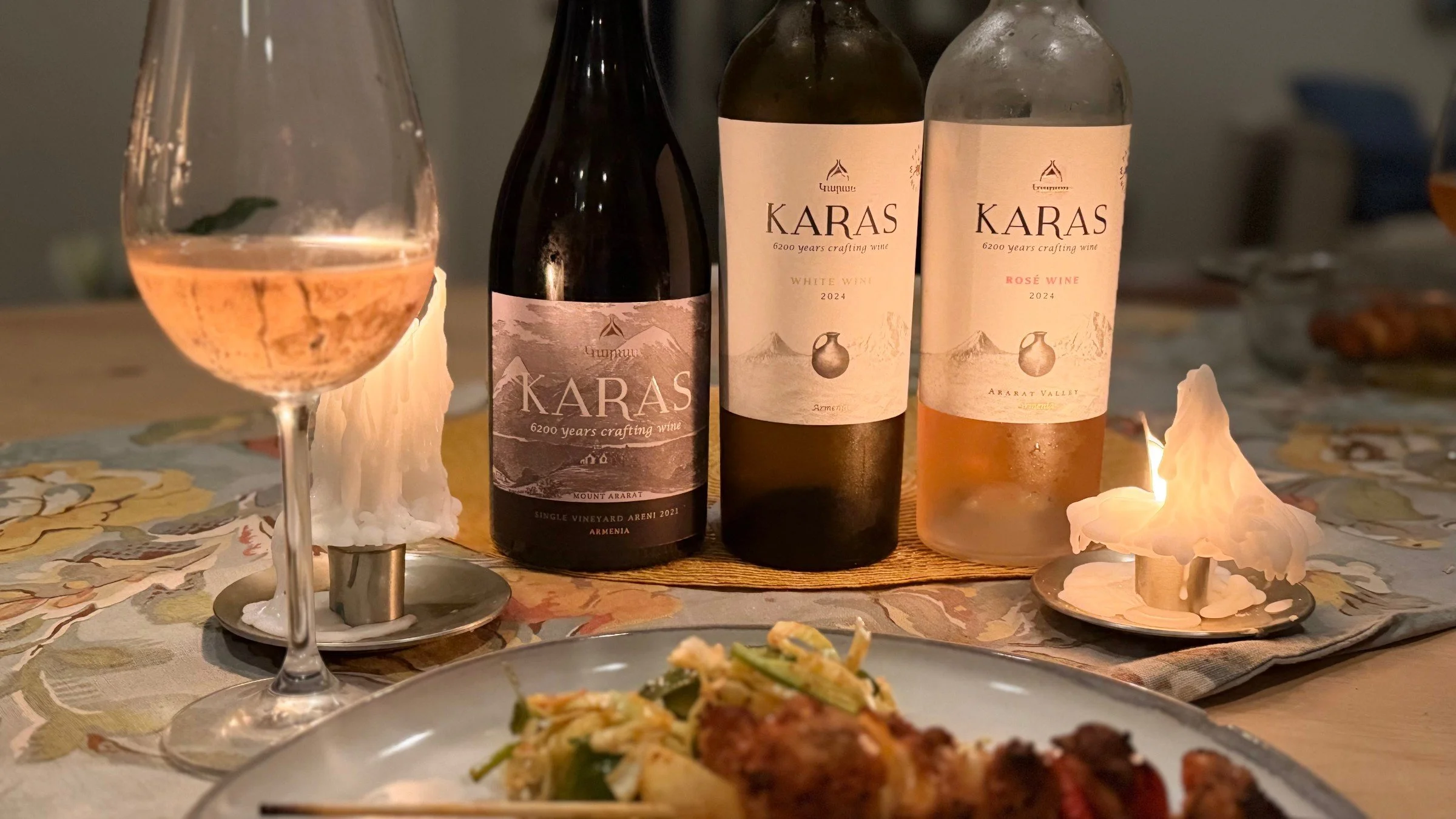 Bottles of Karas wine and a glass of rosé by candlelight beside a plated dish at Bacchus Kitchen + Wine Bar