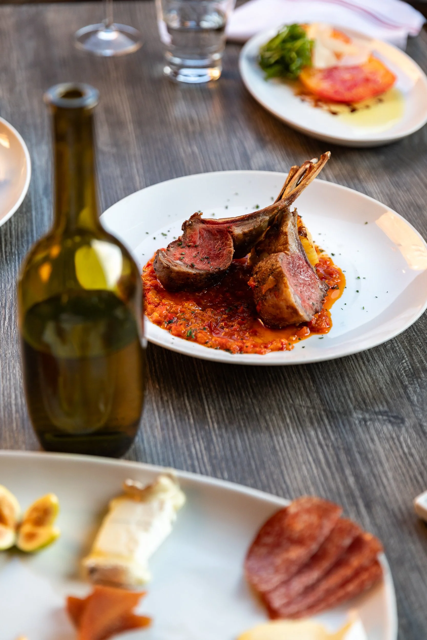 Lamb chops over red sauce next to a bottle of wine at Bacchus