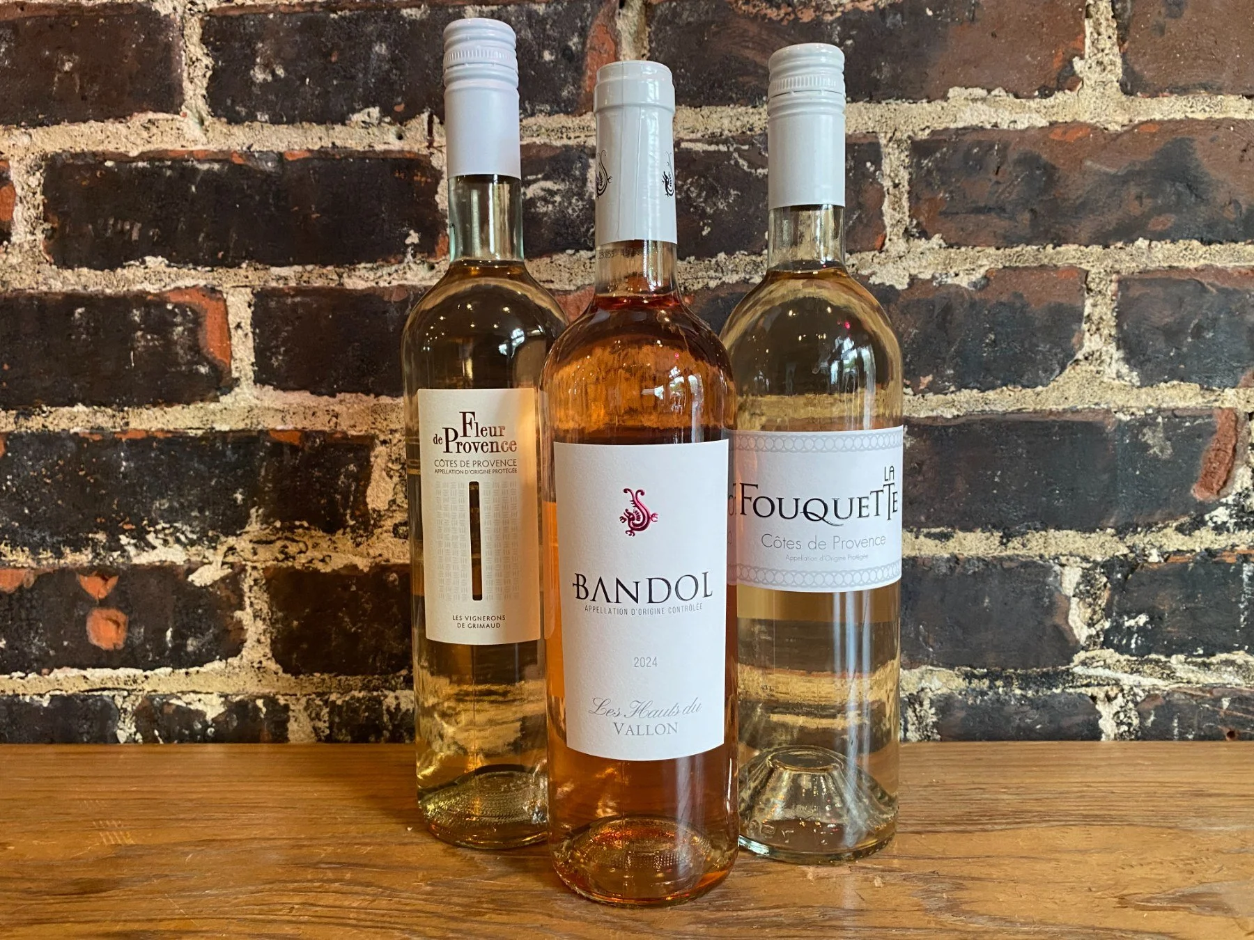 Three white and rosé wines on the bar against a brick wall