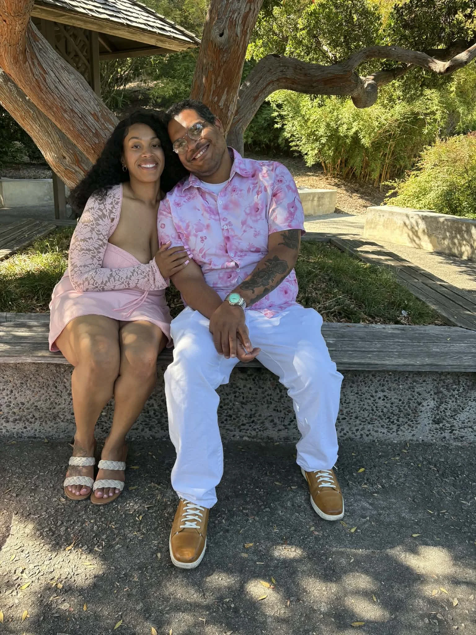 Jazzmin and Sean sitting together on a park bench and smiling at the camera at the huntington library