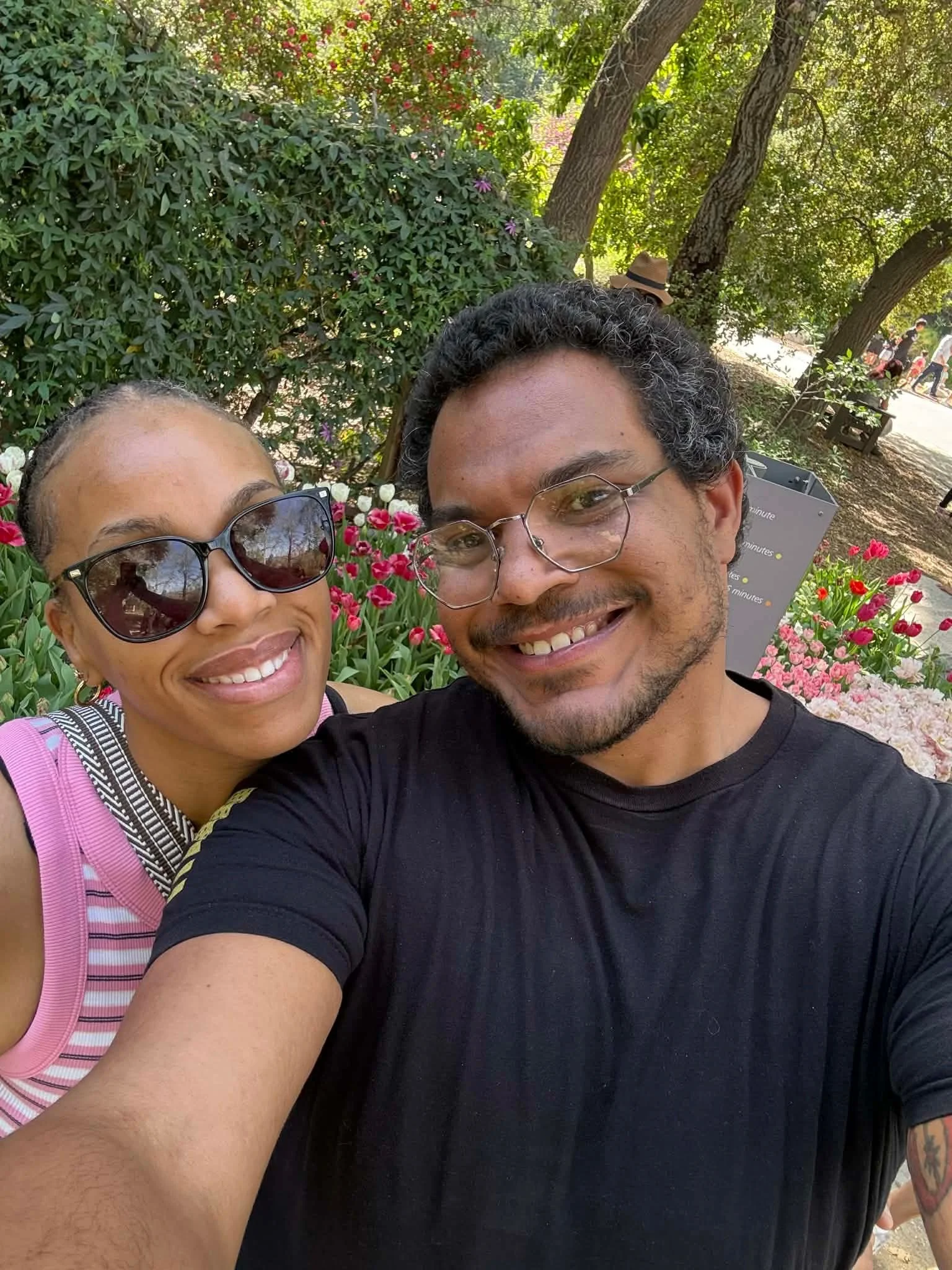 Jazzmin and Sean smiling together among flowers and trees in a park