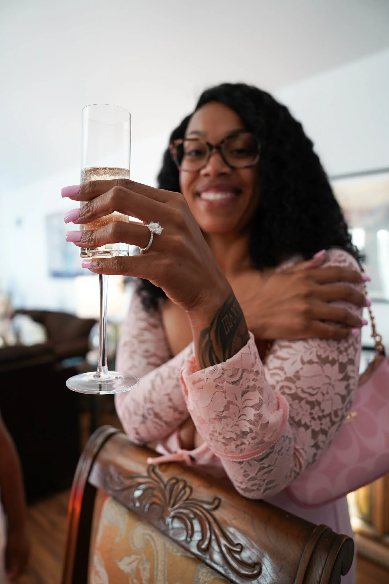 Jazzmin smiling while holding a champagne glass during a celebration, visible engagement ring