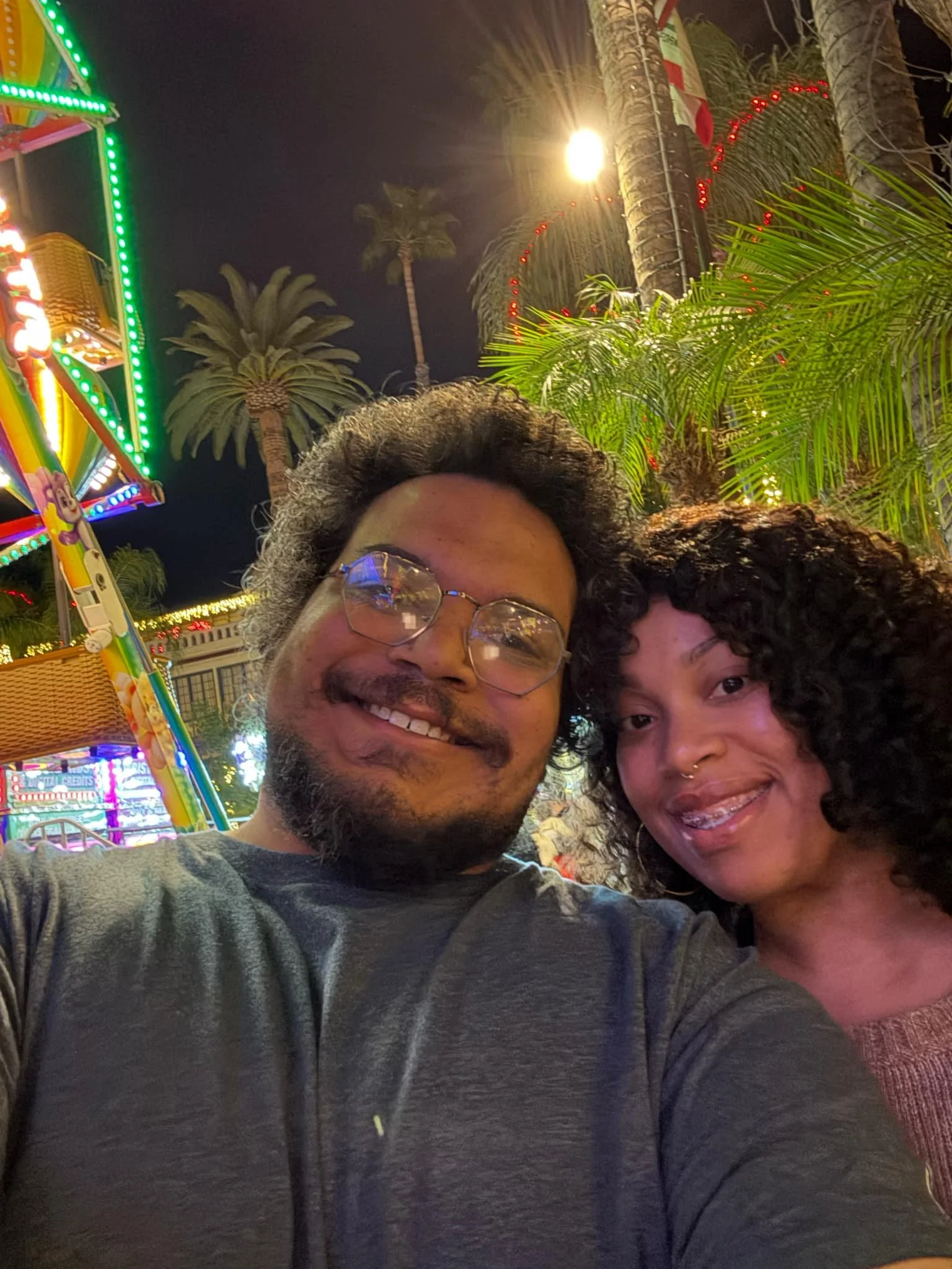 Jazzmin and Sean smiling together during a nighttime visit to an amusement park