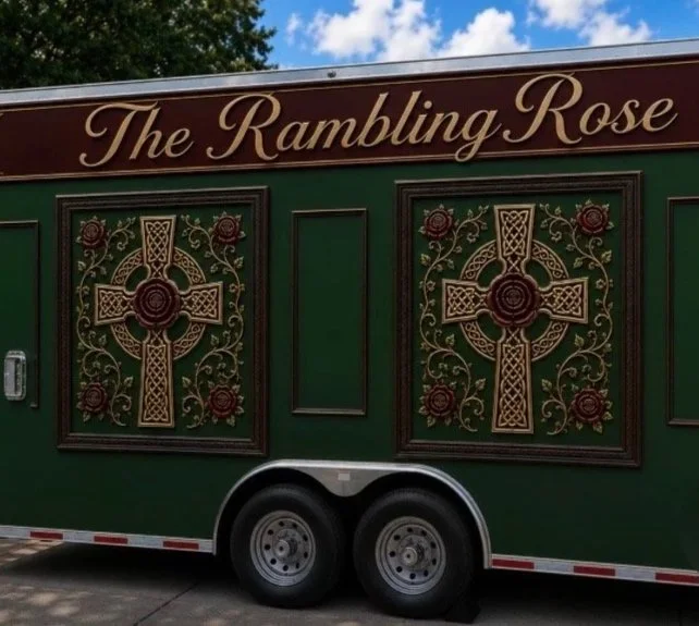 Side view of a green trailer with the text 'The Rambling Rose' and decorative patterns featuring a cross and roses.