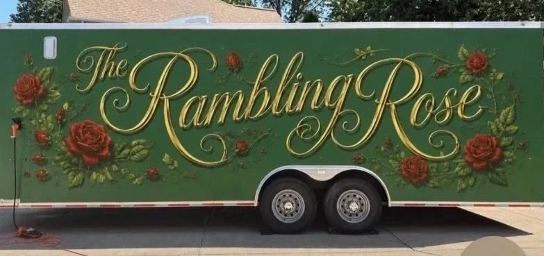 A green trailer decorated with red roses and leaves, with the text "The Rambling Rose" written in elegant yellow script.