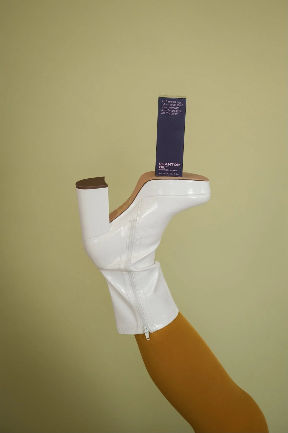 A person's leg wearing orange tights and a white heeled boot with a boxed product balanced on the sole of the boot.