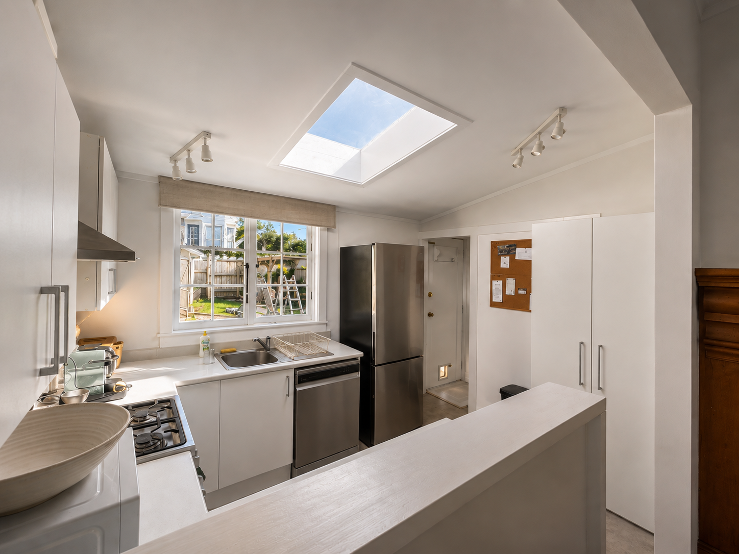 Bright kitchen with white cabinets, stainless steel refrigerator, stovetop, and a window showing a backyard with a swing set.