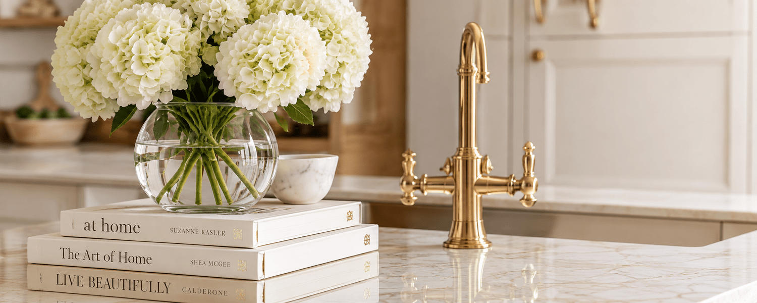 Brass faucet and white hydrangeas on a marble counter