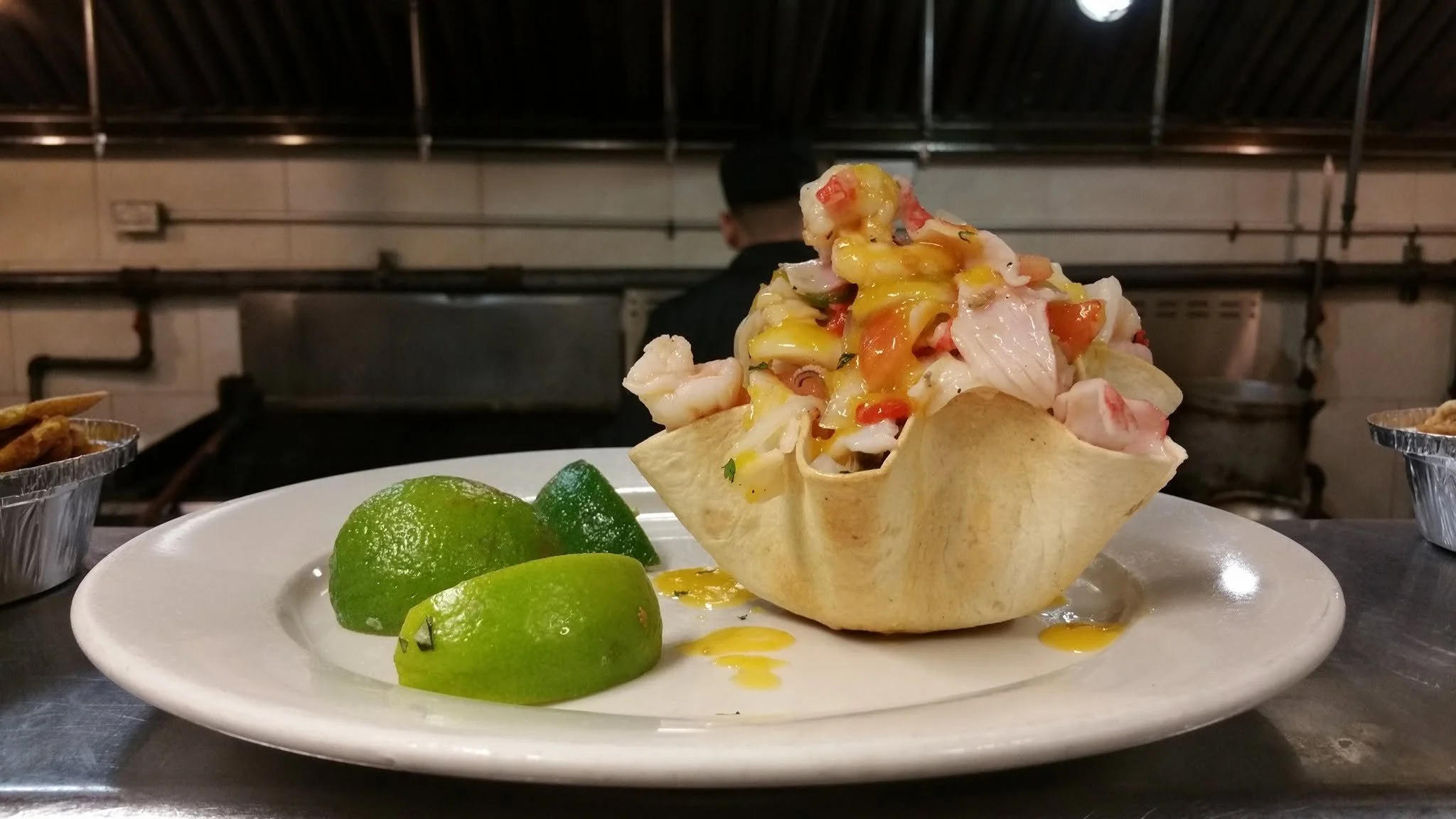 Taco salad served in a crunchy tortilla bowl, topped with shredded lettuce, chopped tomatoes, cheese, and dressing, with lime wedges on the side.