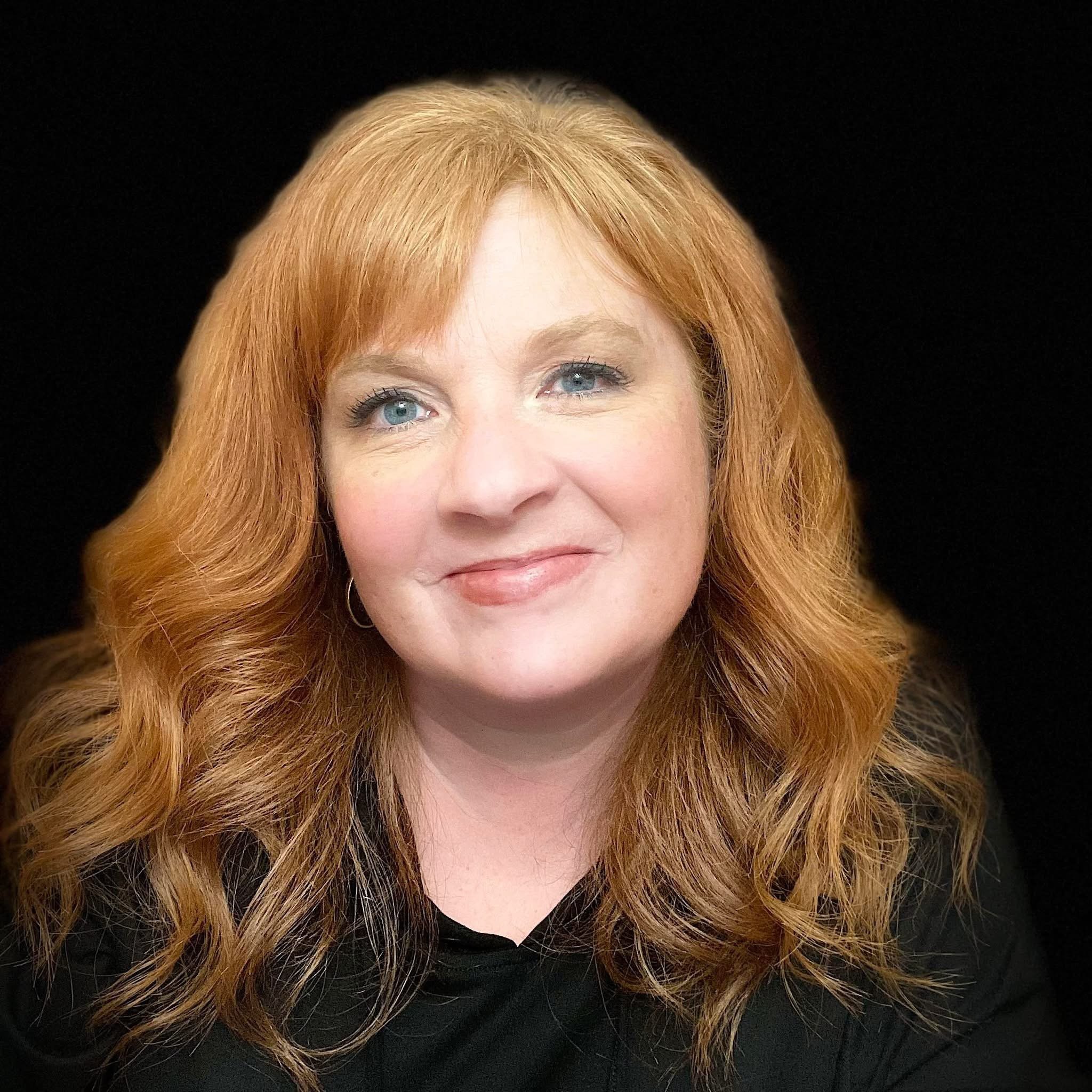 Close-up of a woman with red hair, light skin, and blue eyes, smiling slightly against a black background.