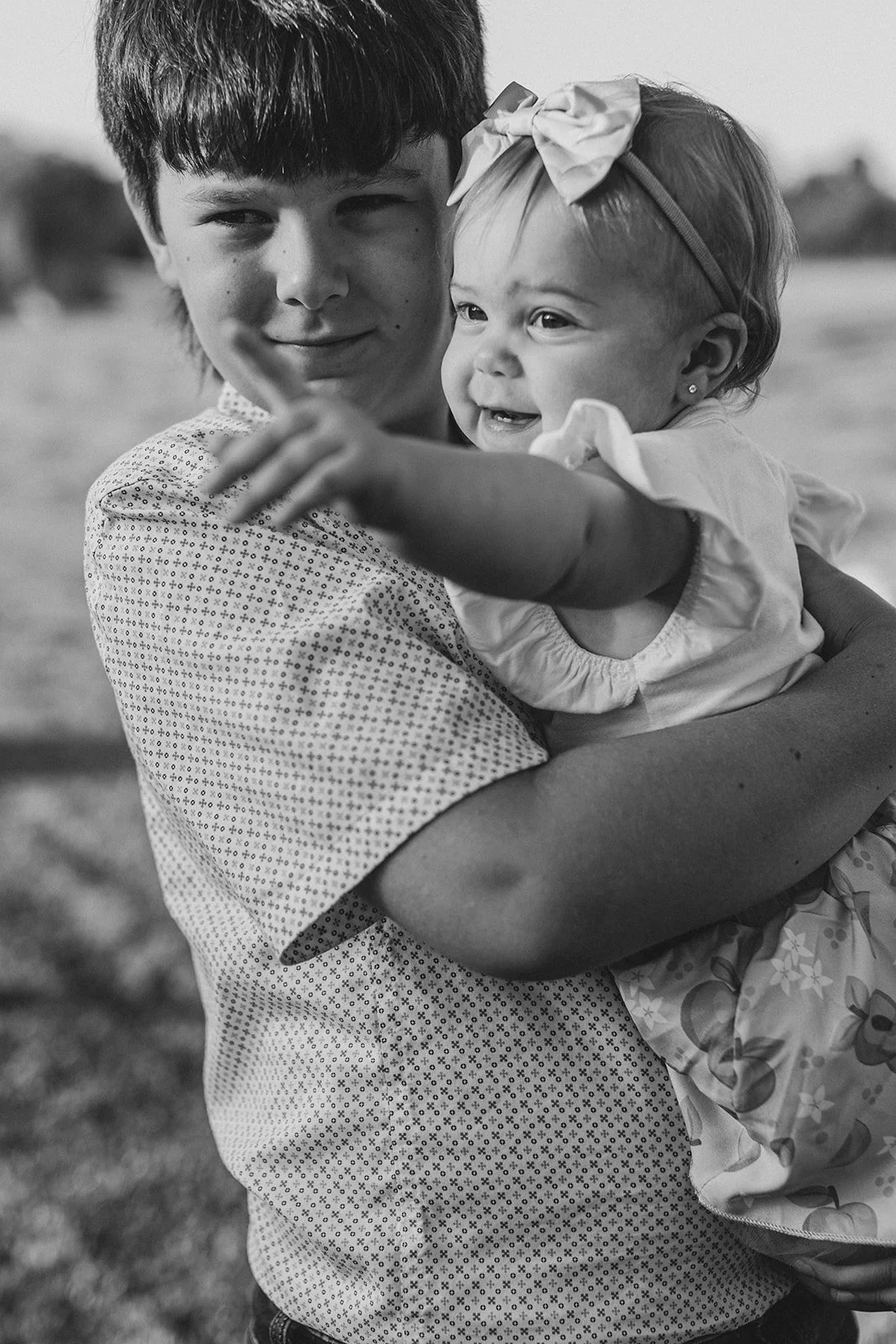 A young man holding a laughing little girl with a bow in her hair, outdoors during daytime.