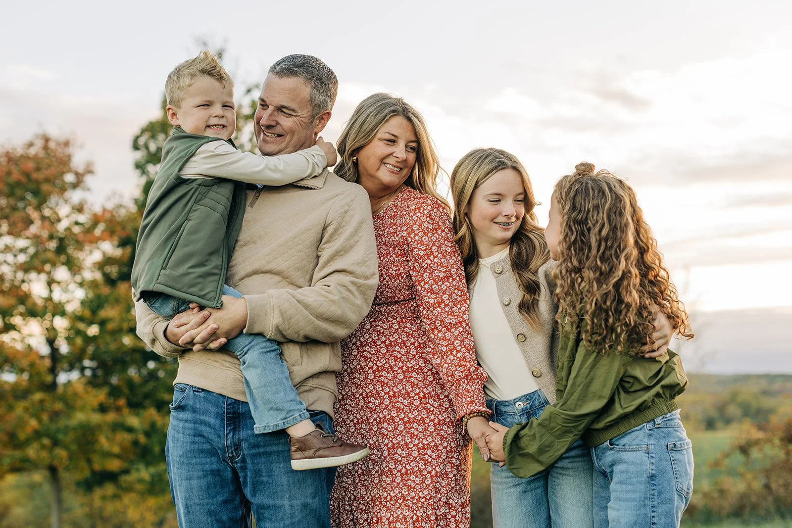 A family of five standing outdoors, smiling and holding hands, with two adults and three children.