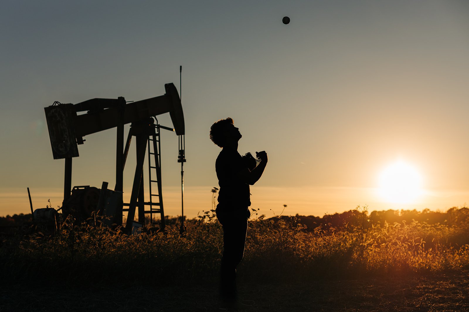 Silhouette of a person holding a camera standing in front of oil pumpjack at sunset. Senior portrait. Senior silhouette.