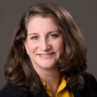 A portrait of a smiling woman with shoulder-length brown hair, wearing a dark blazer and a yellow blouse, against a gray background.