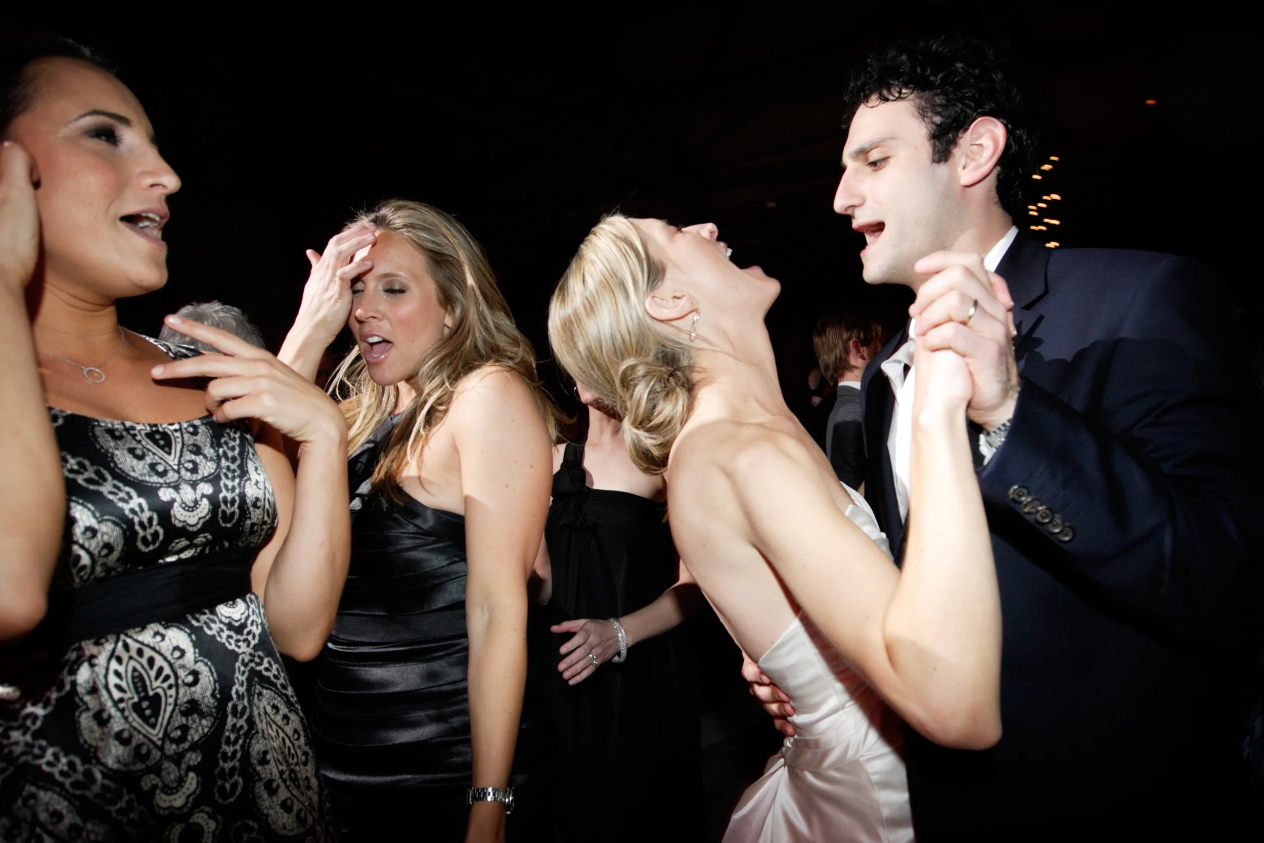 Group of people dancing closely at a party, smiling and enjoying themselves, dressed in formal attire.