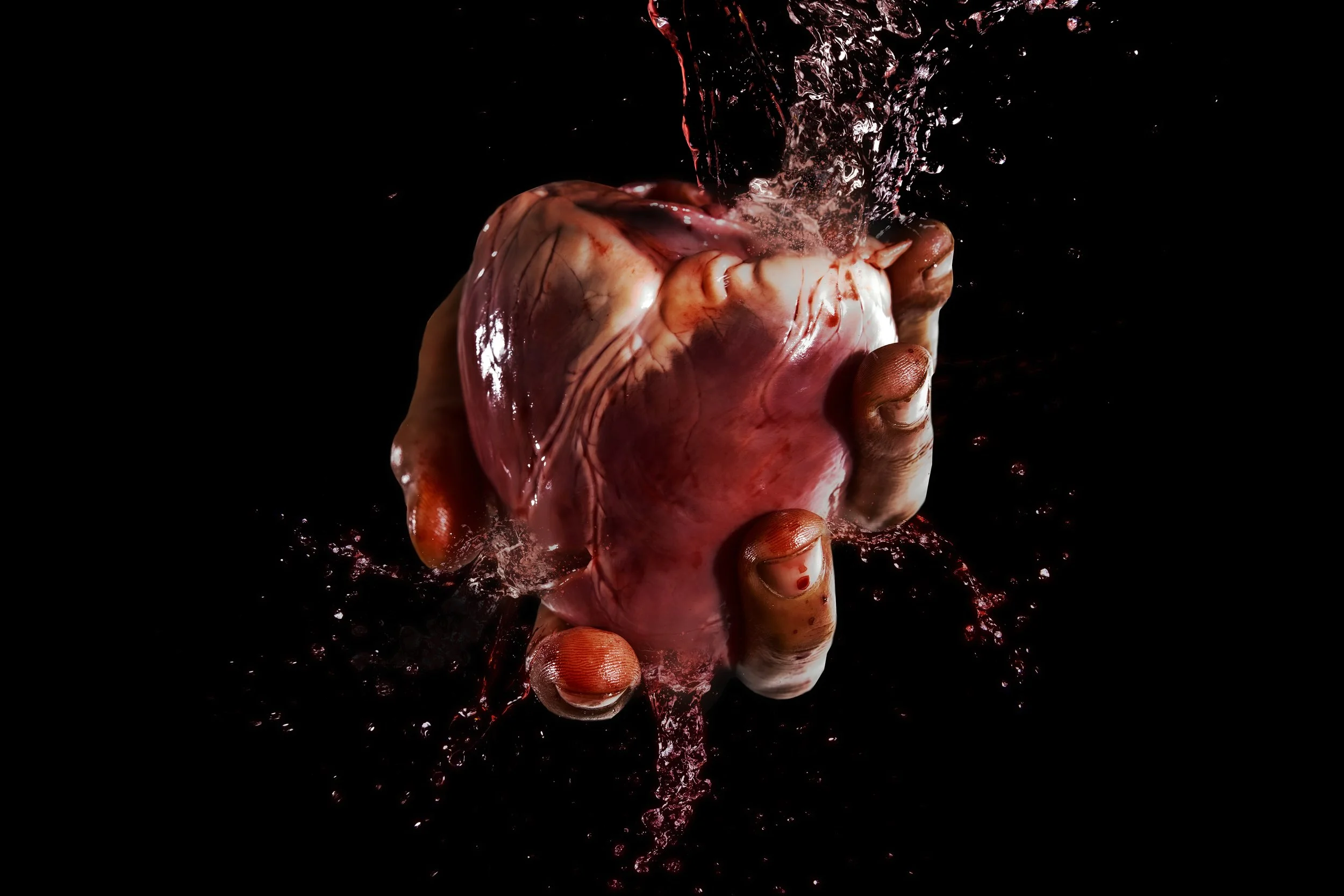 A human heart held in a hand with water splashing around and falling onto it against a black background.