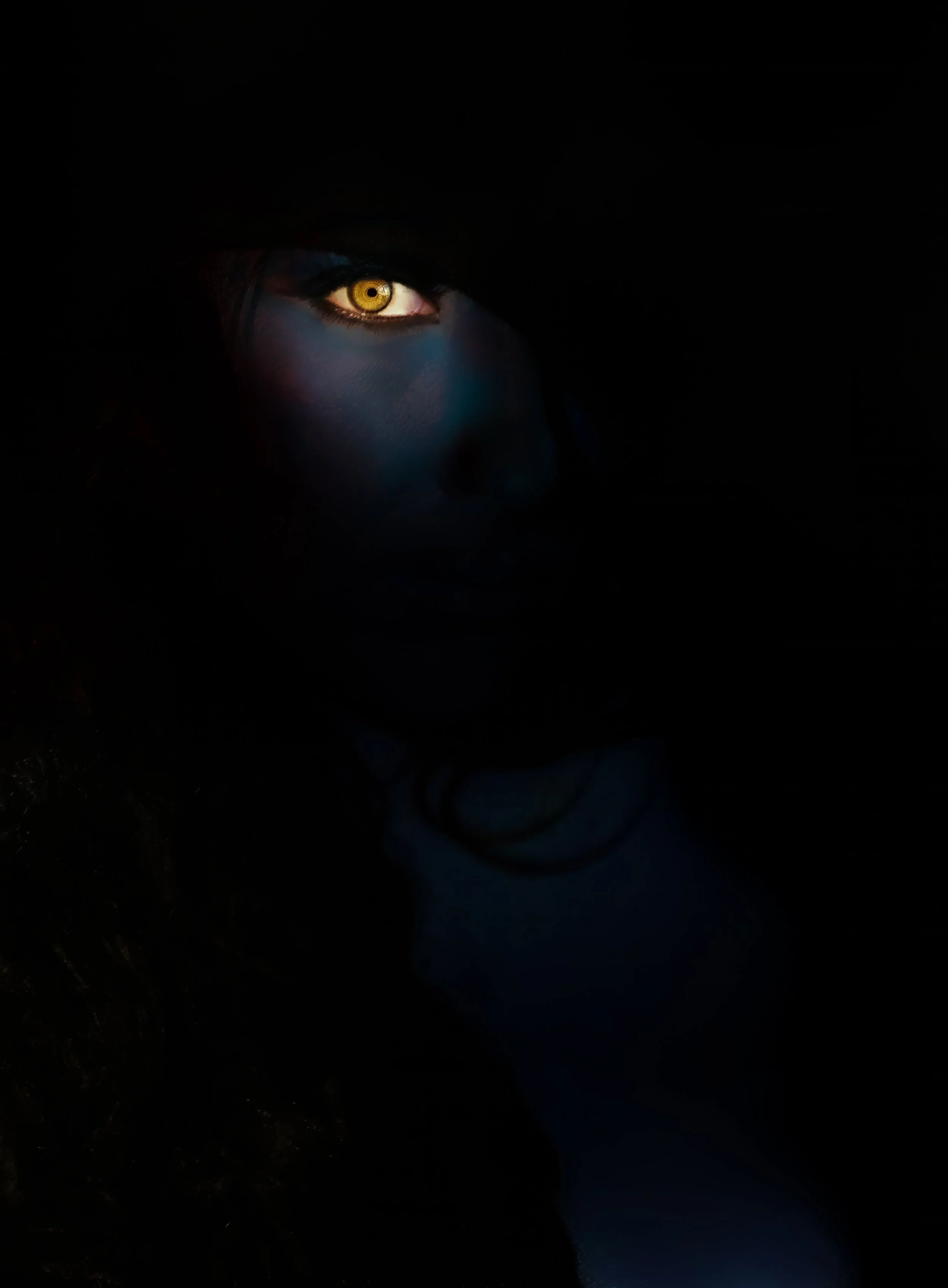 Close-up of a woman's face illuminated in dark surroundings, with a focus on her left eye that appears to glow gold.